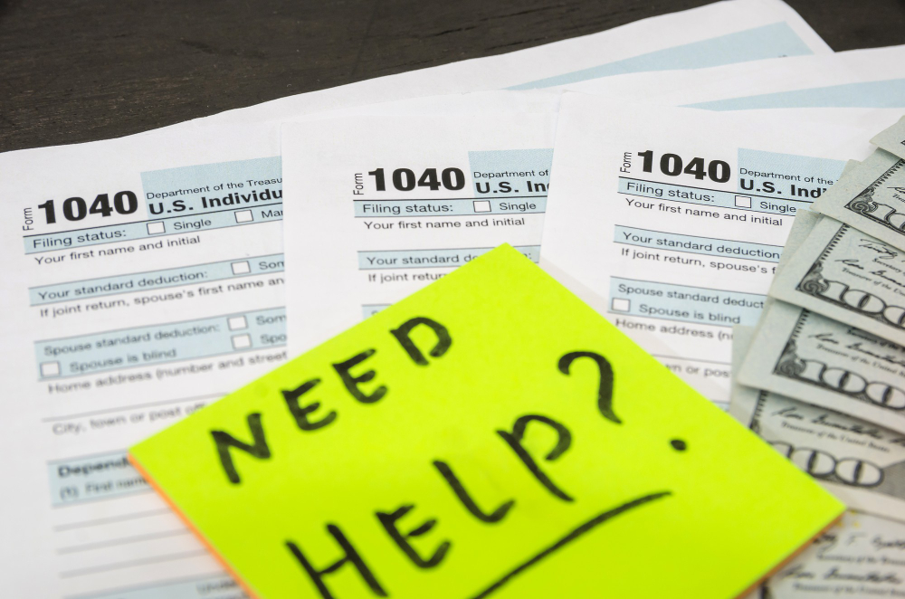 IRS tax forms 1040 with cash and note saying need help, representing tax issues.