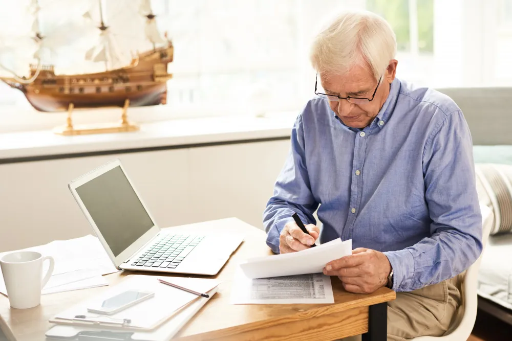 Senior man reviewing retirement income and tax documents at home.