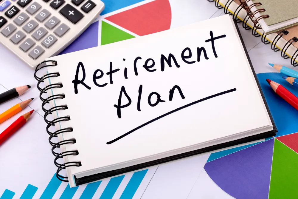 Retirement plan written in notebook with financial charts and calculator on desk.