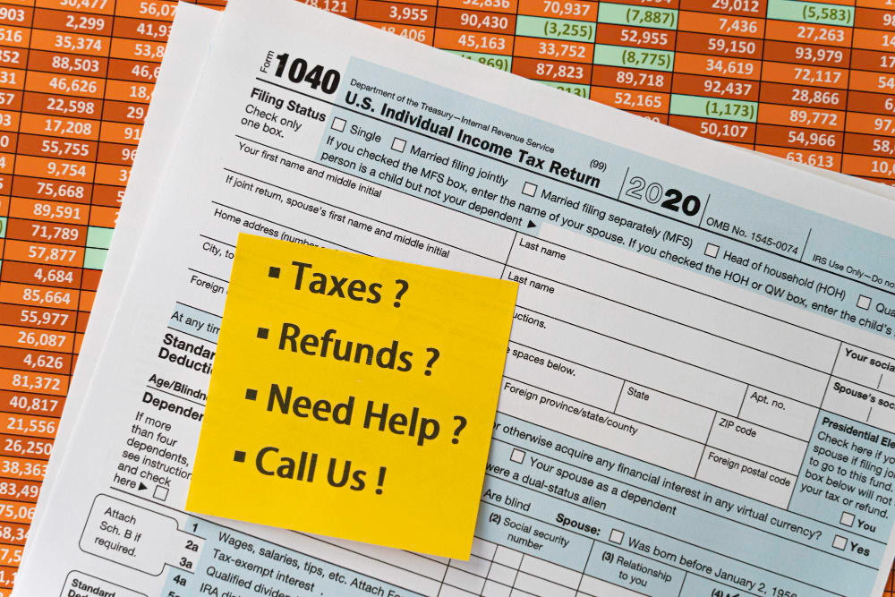 Federal income tax return form with financial spreadsheet background and a yellow sticky note listing tax help topics, including taxes, refunds, and filing assistance.