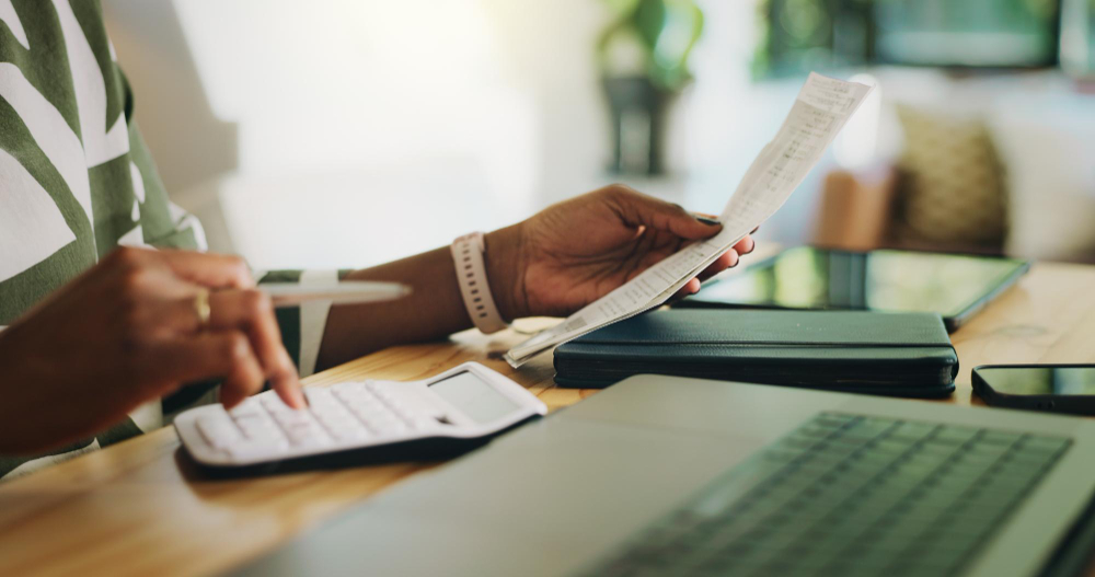 Person reviewing financial documents with a calculator and laptop