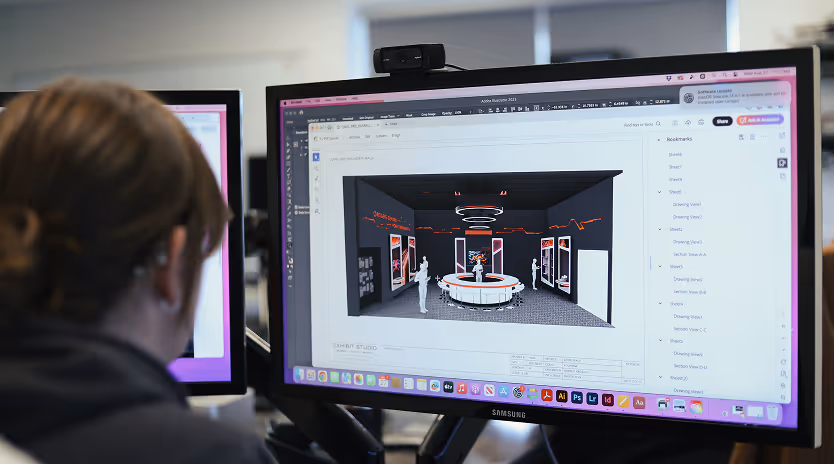 Person viewing a 3D interior design of a showroom with mannequins and circular display table on a computer monitor.