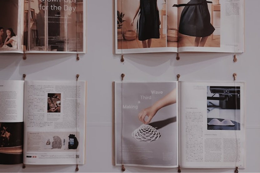 Six open magazines pinned to a wall, displaying fashion photos, text, and a hand interacting with a spiral object.