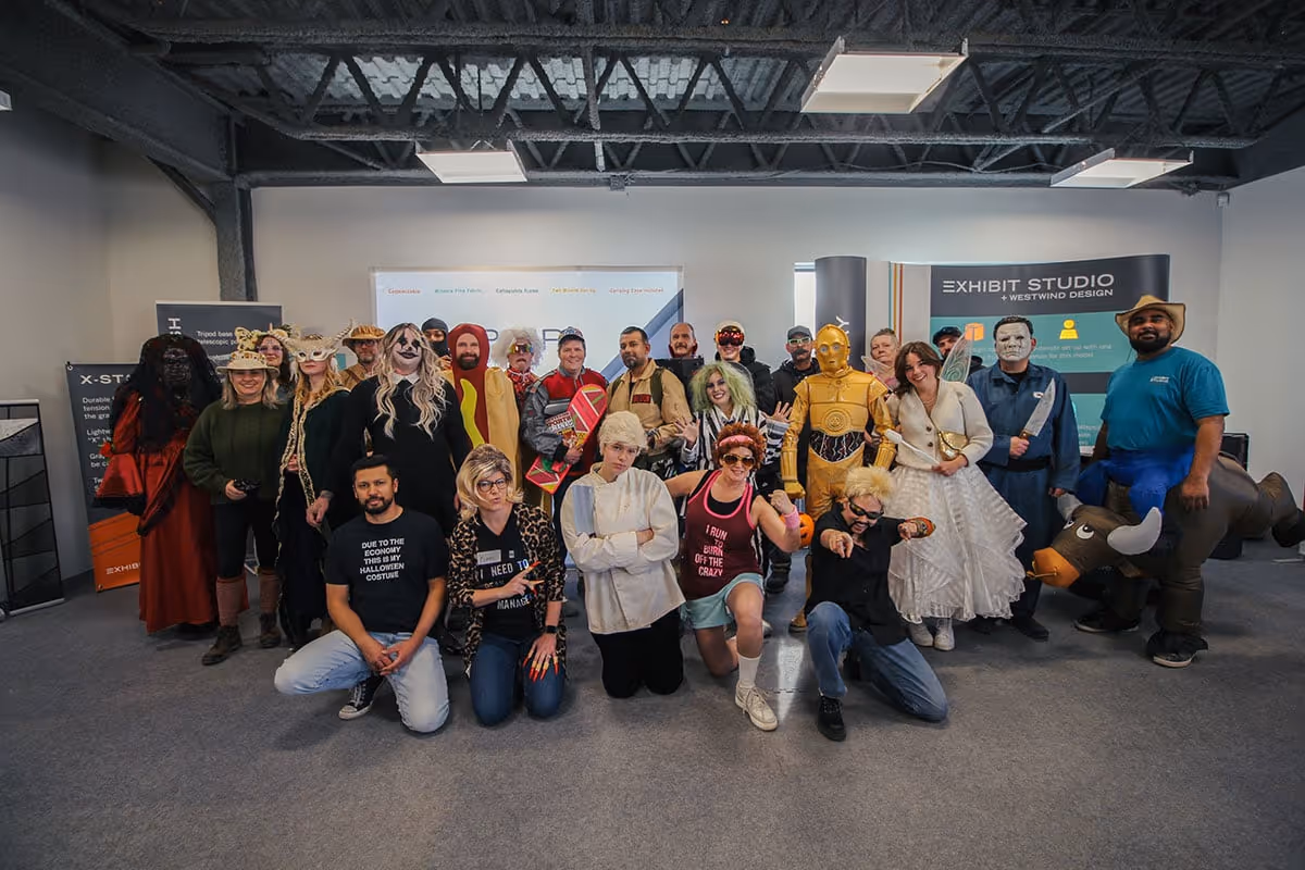 Group of people dressed in various Halloween costumes posing indoors in an office setting.