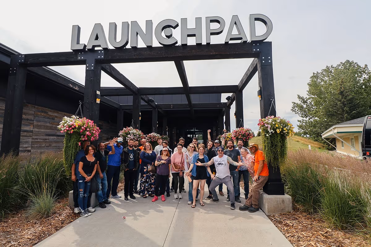 Group of people standing and posing happily under a black wooden entrance structure with large letters spelling 'LAUNCHPAD'.