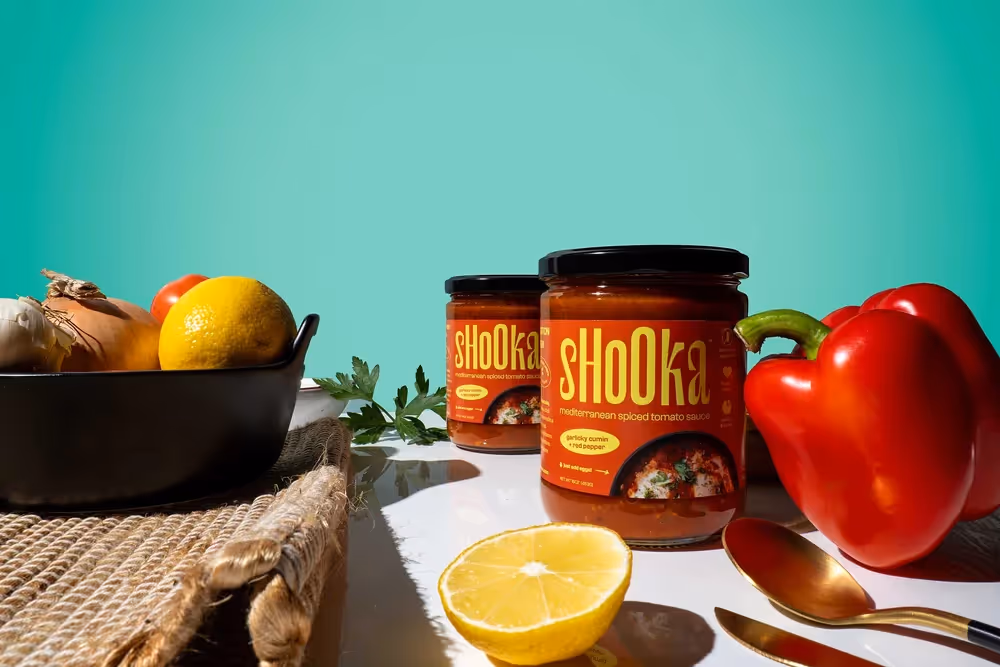 Shooka sauce jar with lemons and utensils on teal table scene, food photography by Photos by Lars.