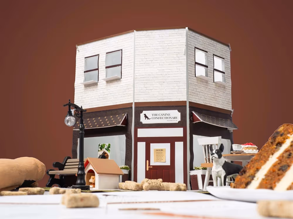 Mini storefront model on tabletop with warm brown backdrop and scattered props, product photography by Photos by Lars.