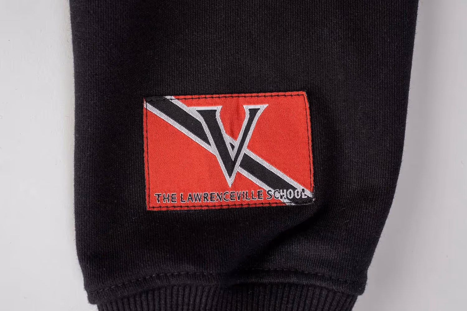 Red V patch on black cuff with striped trim on white background, apparel photography by Photos by Lars.