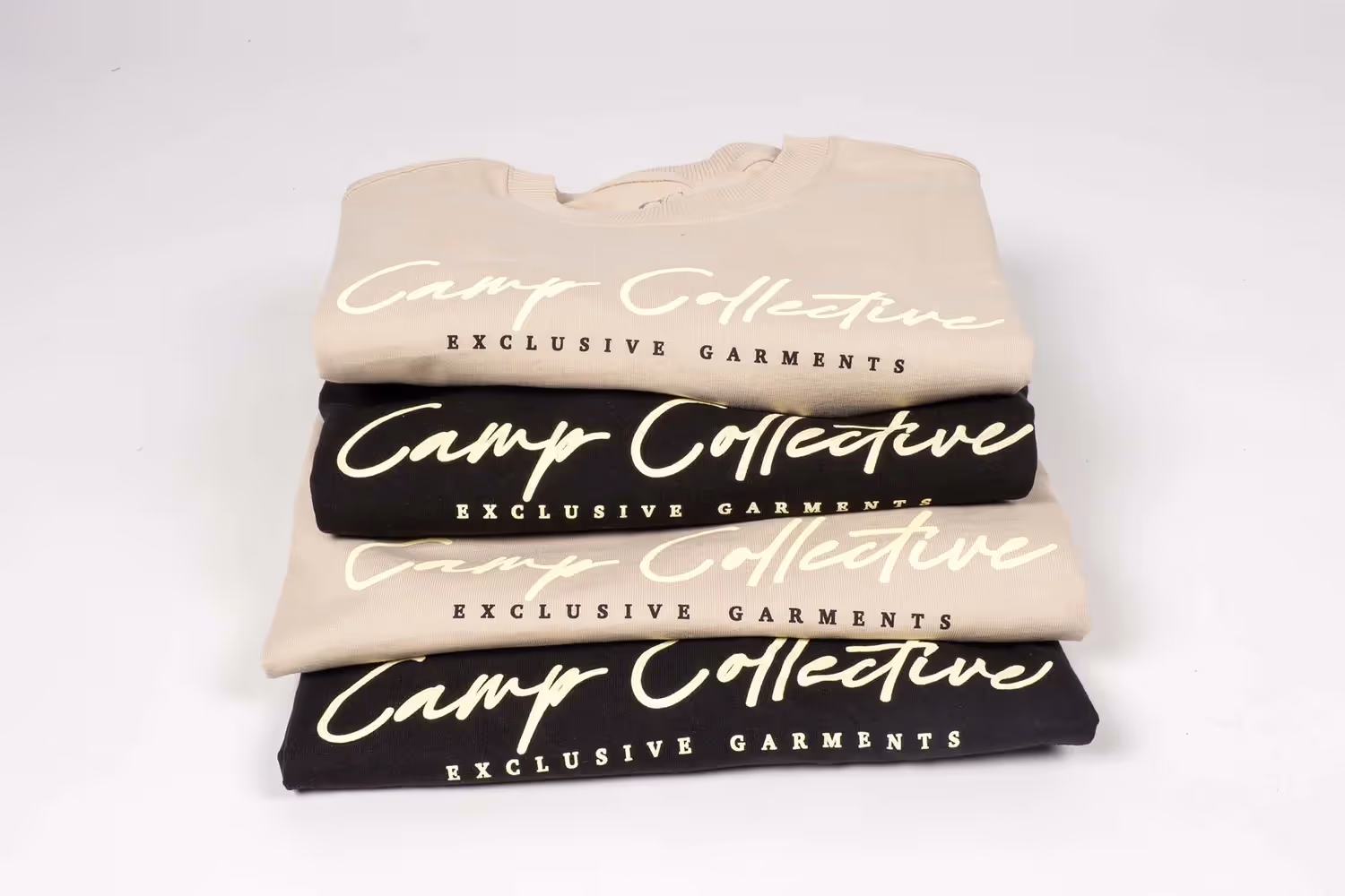 Stack of folded Camp Collective shirts in black and beige on white, ecommerce photography by Photos by Lars.