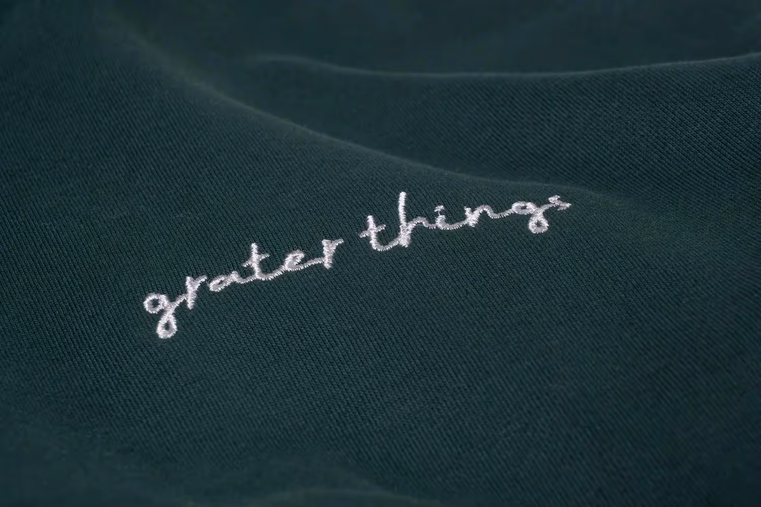 Close-up embroidery reading 'greater things' on green fabric, apparel detail photography by Photos by Lars.