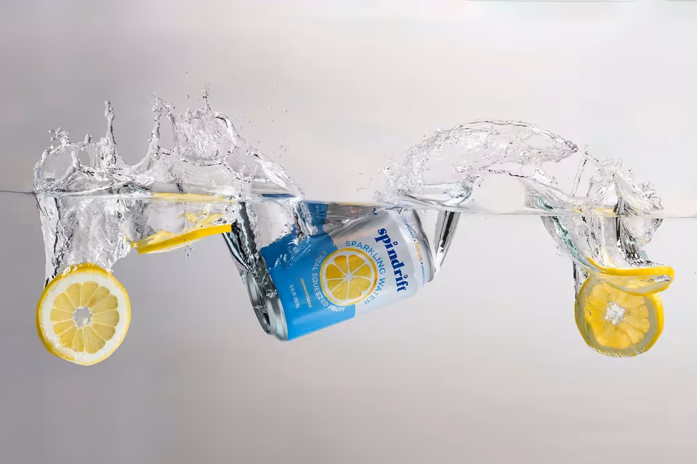 Spindrift Lemon can splashing through water with lemon slices on gray backdrop, beverage product photography by Photos by Lars.