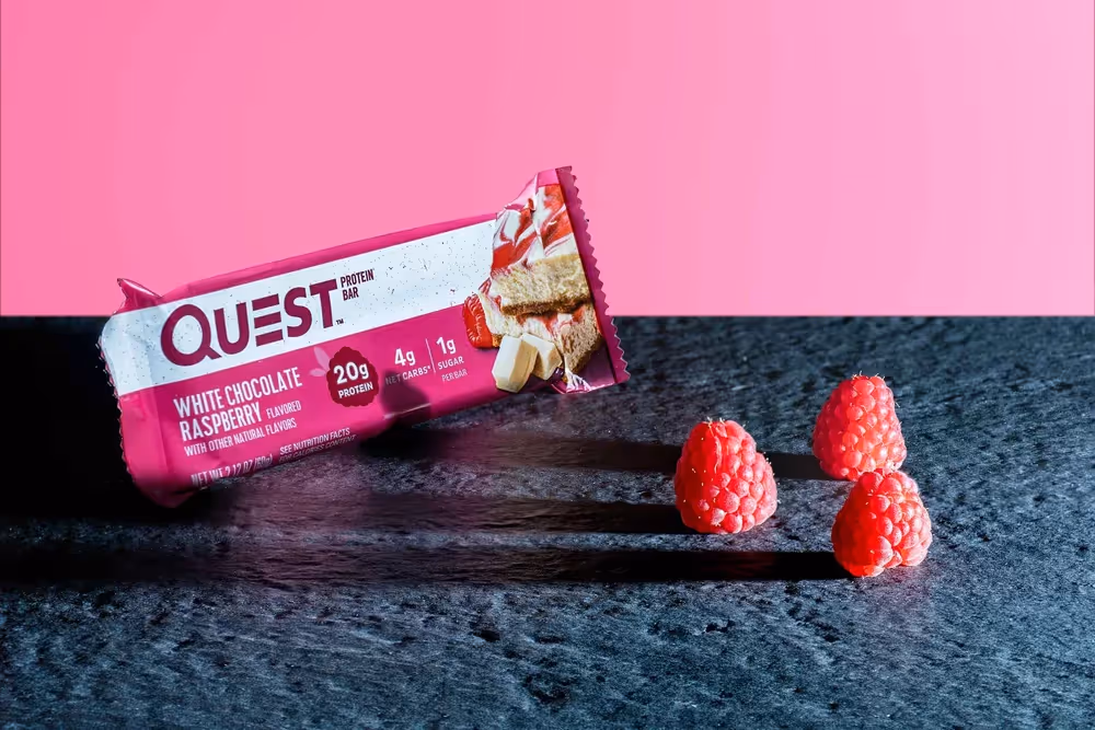 Quest bar on dark slate with raspberries beside wrapper, ecommerce food photography by Photos by Lars.