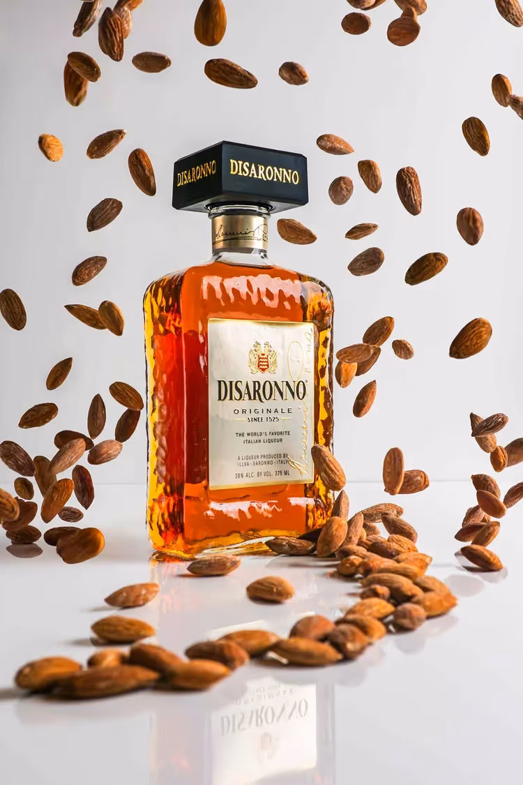 Disaronno bottle surrounded by falling almonds on white, product photography by Photos by Lars.