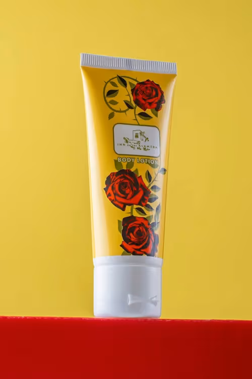 Floral body lotion tube standing on red ledge against yellow background, studio product photography by Photos by Lars.