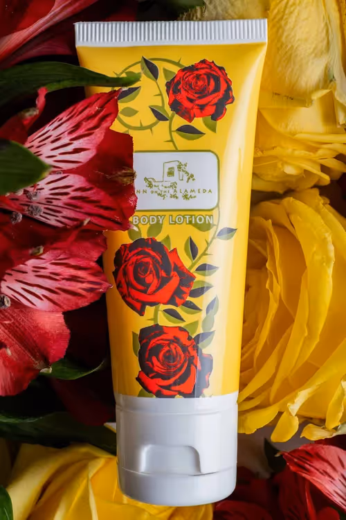 Floral body lotion tube framed by red flowers and yellow fabric, beauty product photography by Photos by Lars.