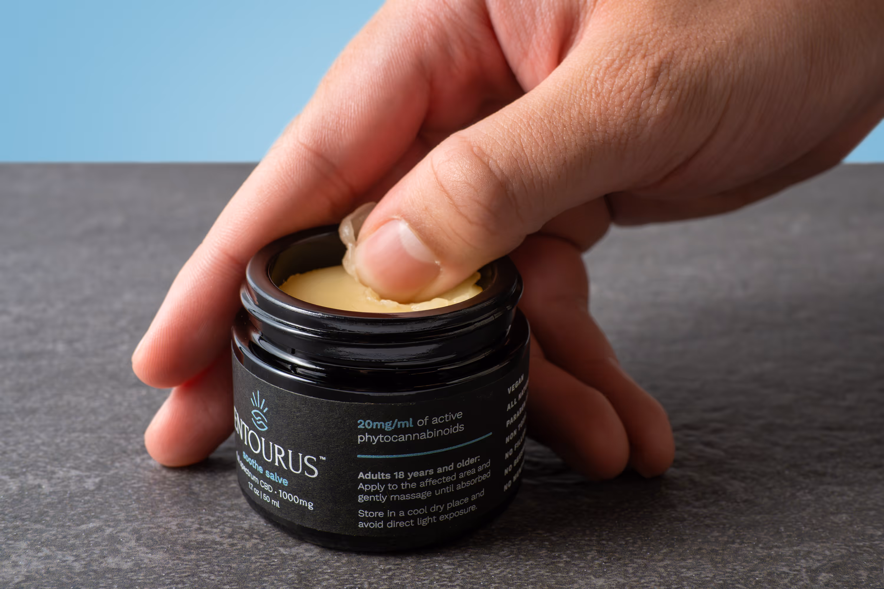 Entourus salve jar on dark surface as a finger presses the cream, product photography by Photos by Lars.