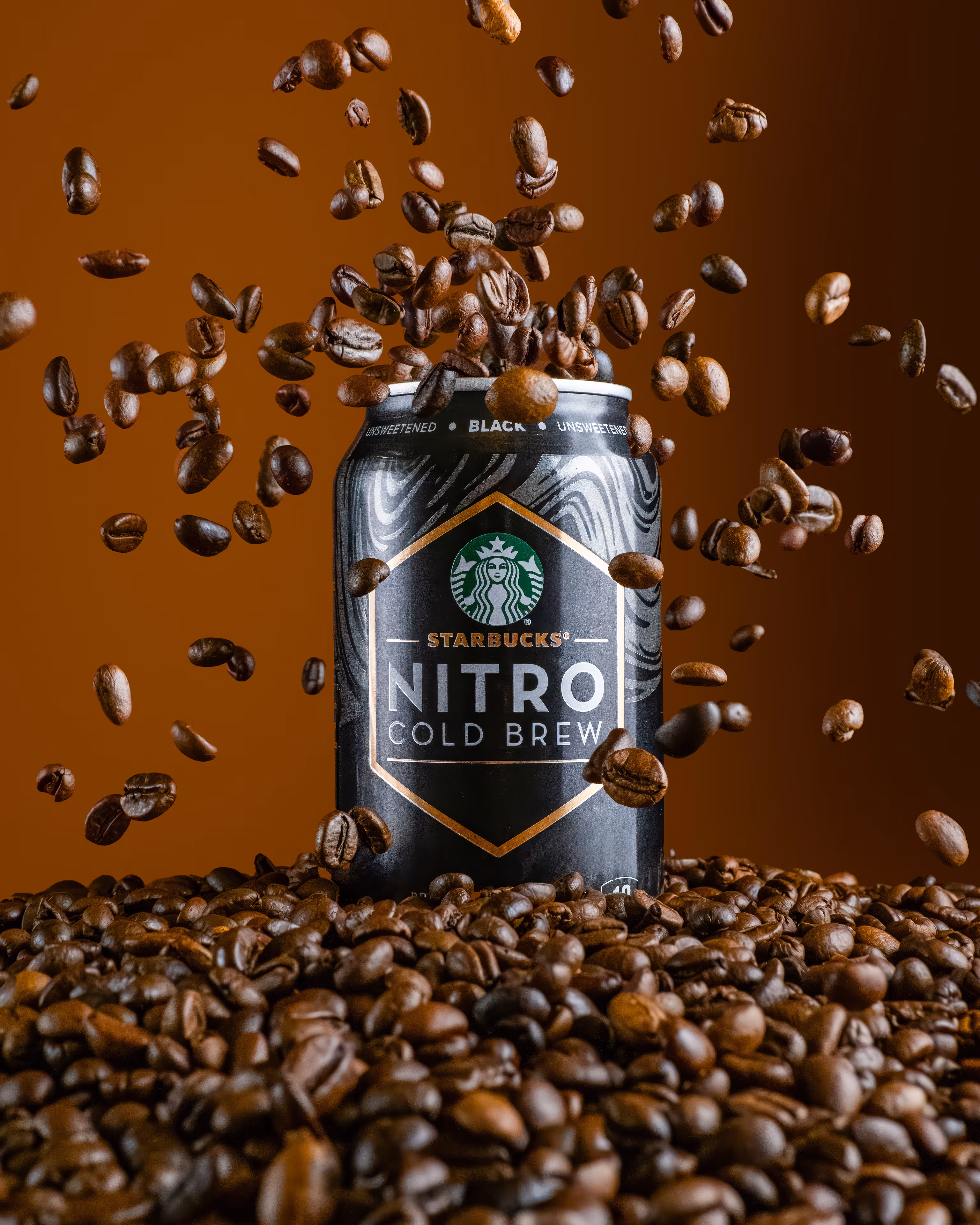 Starbucks Nitro Cold Brew can surrounded by flying coffee beans over a bean pile, food photography by Photos by Lars.