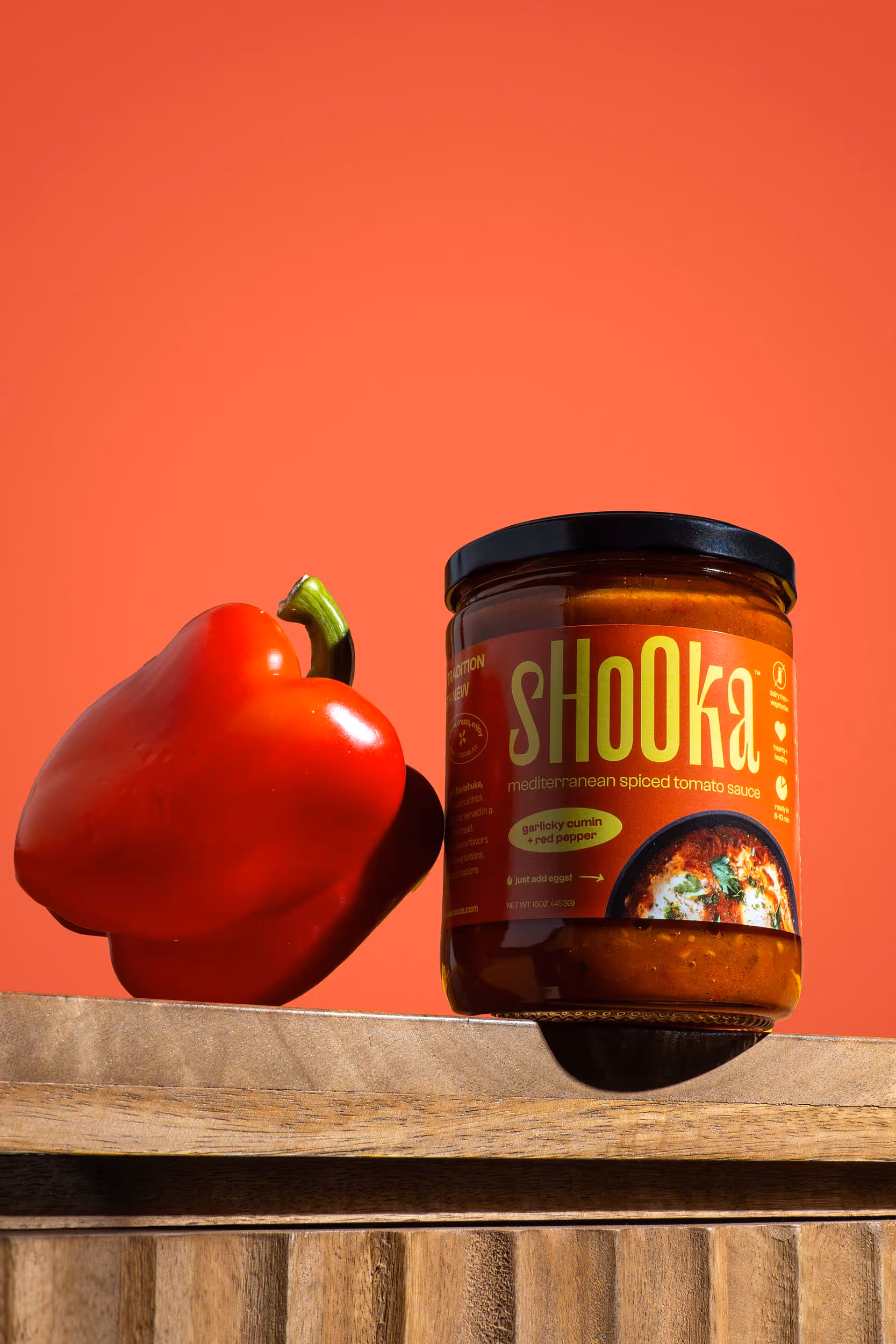 Shooka jar beside a red bell pepper on orange background, product photography by Photos by Lars.