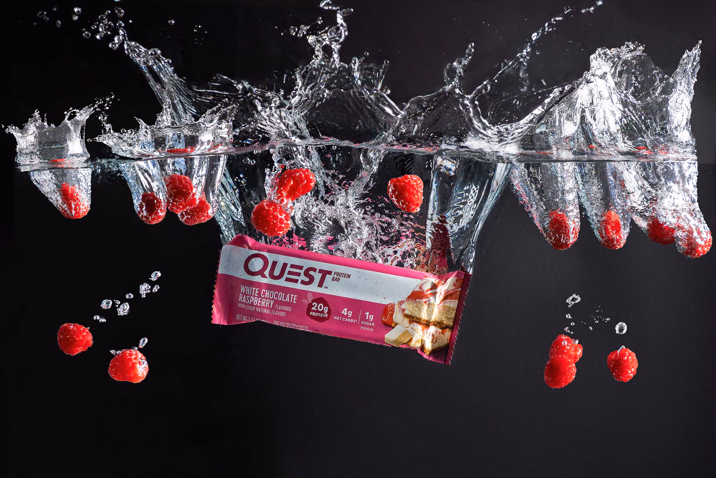 Quest protein bar splashing through water with red berries on black background, product photography by Photos by Lars.