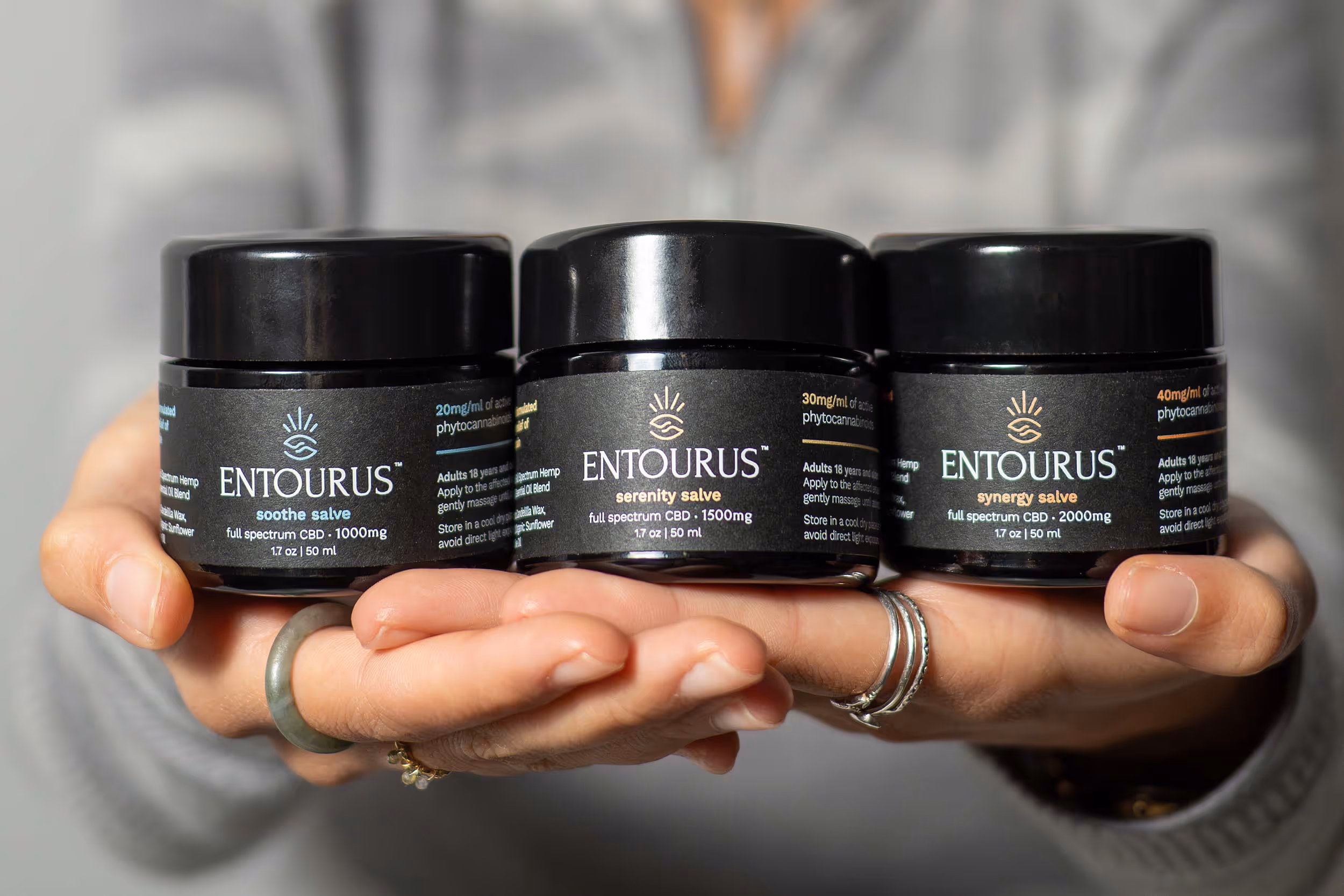 Hands holding three Entourus black skincare jars with silver lids, product photography Photos by Lars