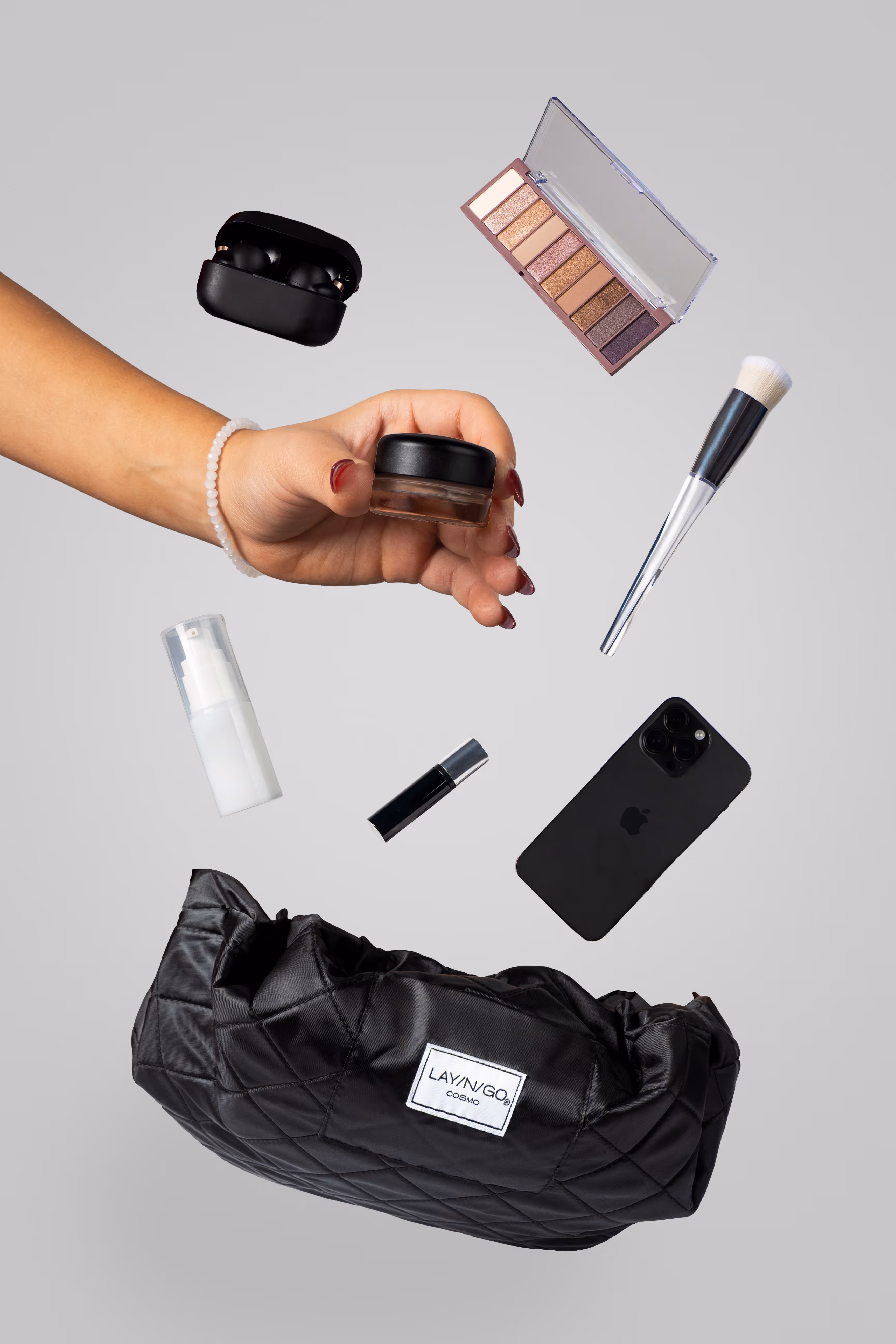 Flat lay of cosmetics, black drawstring bag, and a hand holding a jar, product photography by Photos by Lars.