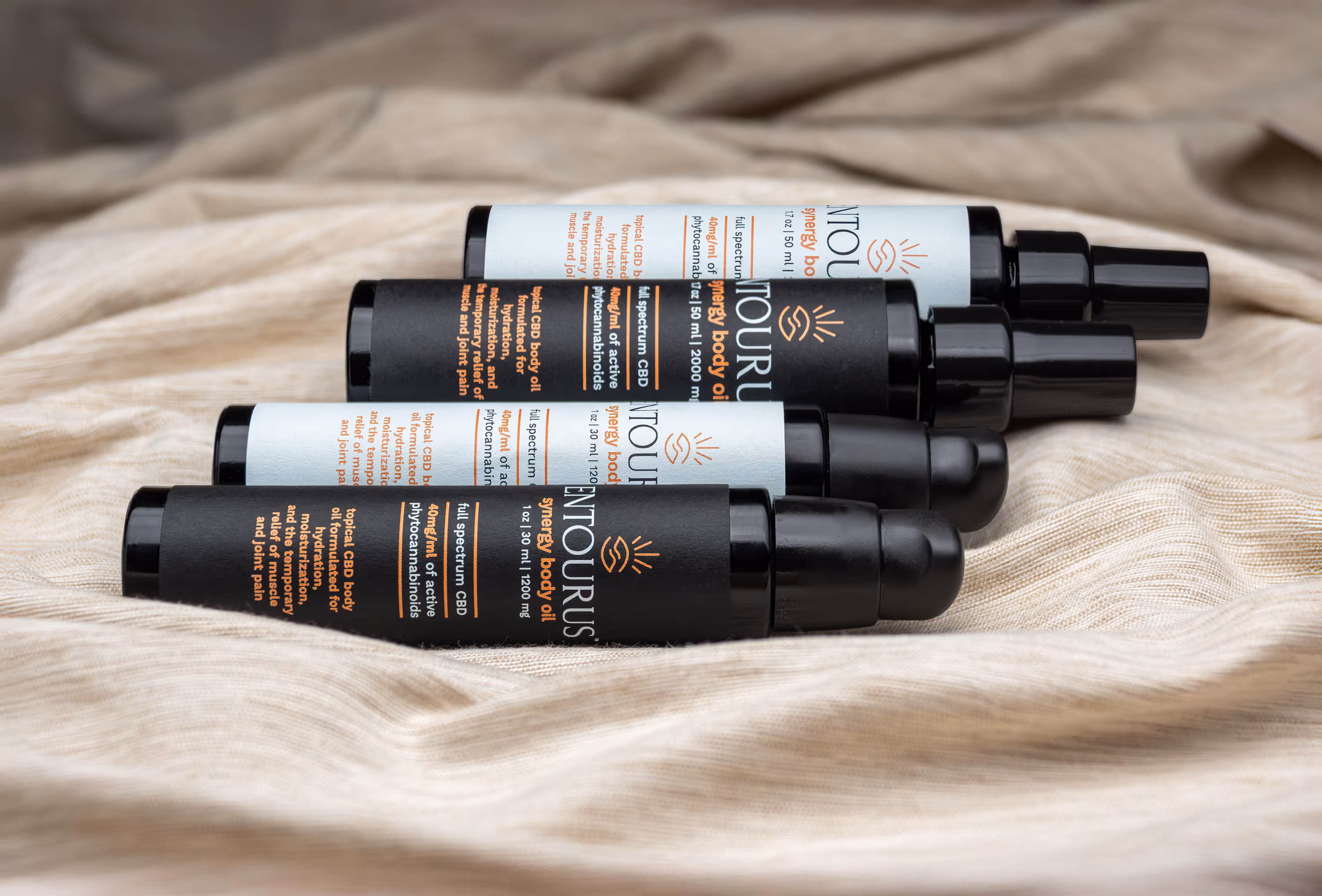 Three Entourus spray bottles on beige linen with soft shadows, beauty product photography Photos by Lars