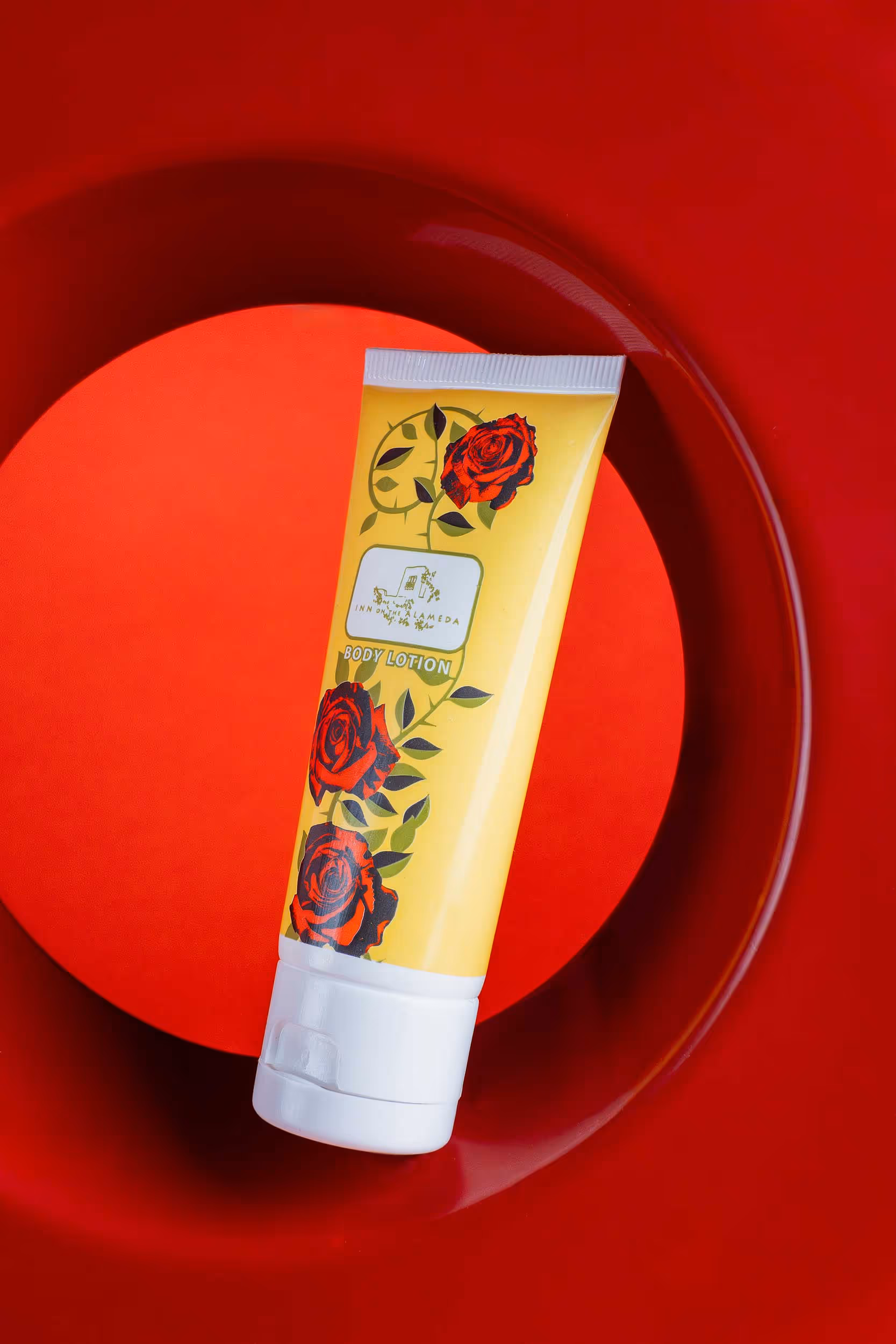 Yellow rose-printed cream tube on red plate against red background, beauty product photography Photos by Lars