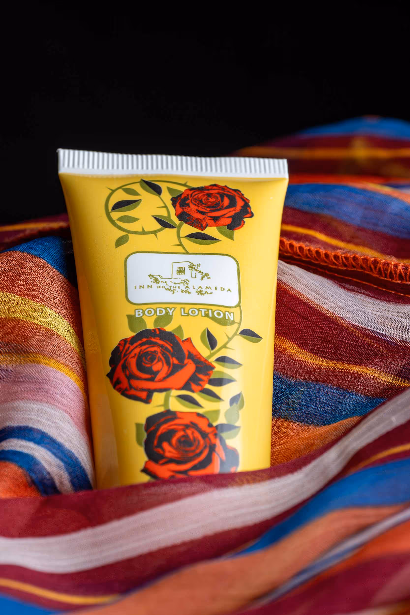 Yellow cream tube with red rose illustrations on colorful striped fabric, product photography Photos by Lars