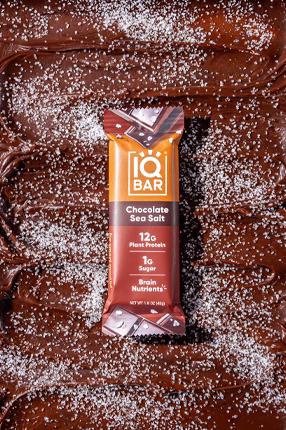 Brown sugar cubes cascade around a Südzucker box labeled "Brauner Würfel Rohrzucker." The scene conveys a playful, dynamic energy.