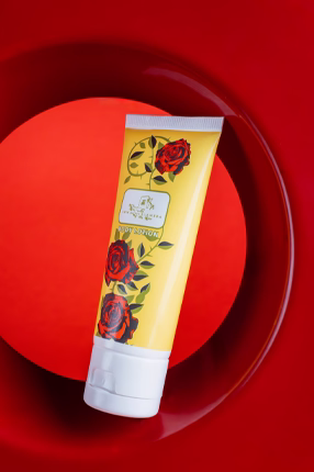 A yellow lotion tube with red roses design stands against a bold red circular background, conveying elegance and luxury in skincare packaging.