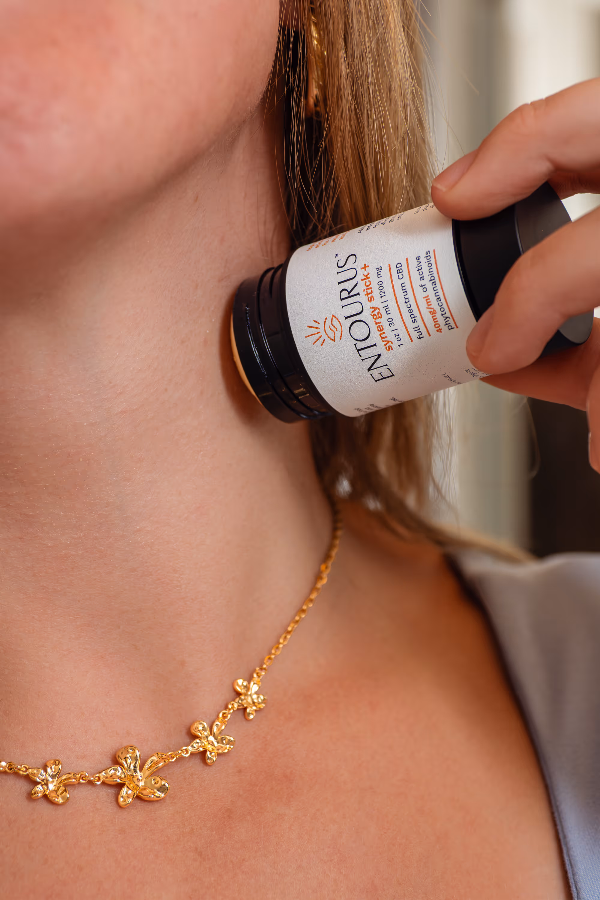 Hand applies Entourus synergy stick to neck, close-up with gold necklace, lifestyle product photography, Photos by Lars.
