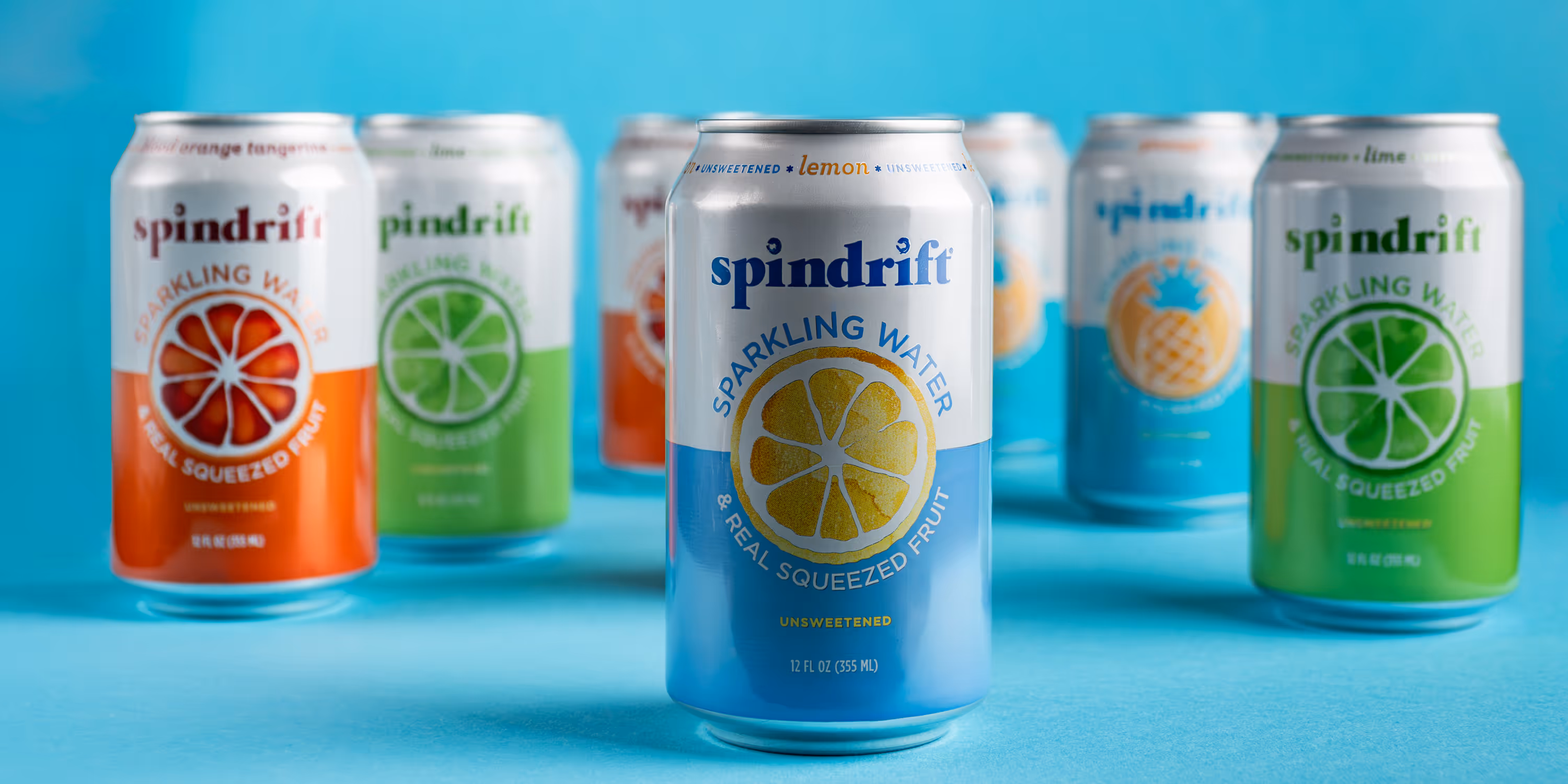 Spindrift Lemon sparkling water can centered with other flavors behind on blue backdrop, CPG product photo, Photos by Lars.