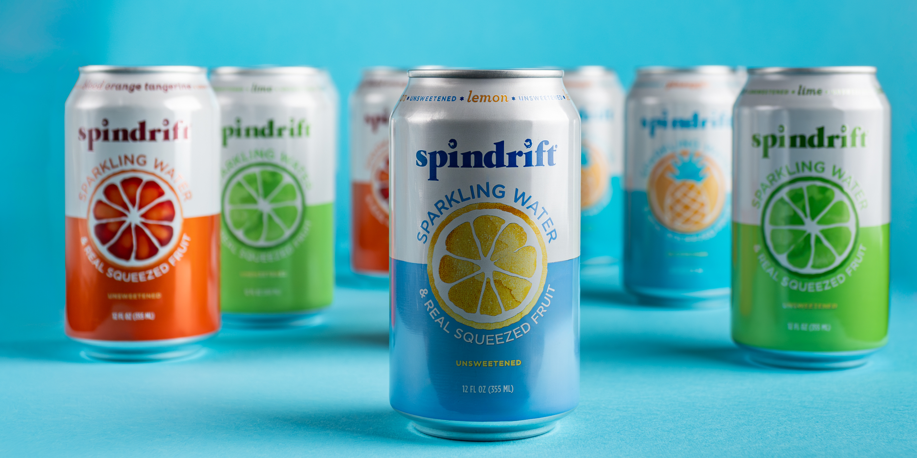 Spindrift Lemon sparkling water can centered with other flavors behind on blue backdrop, CPG product photo, Photos by Lars.