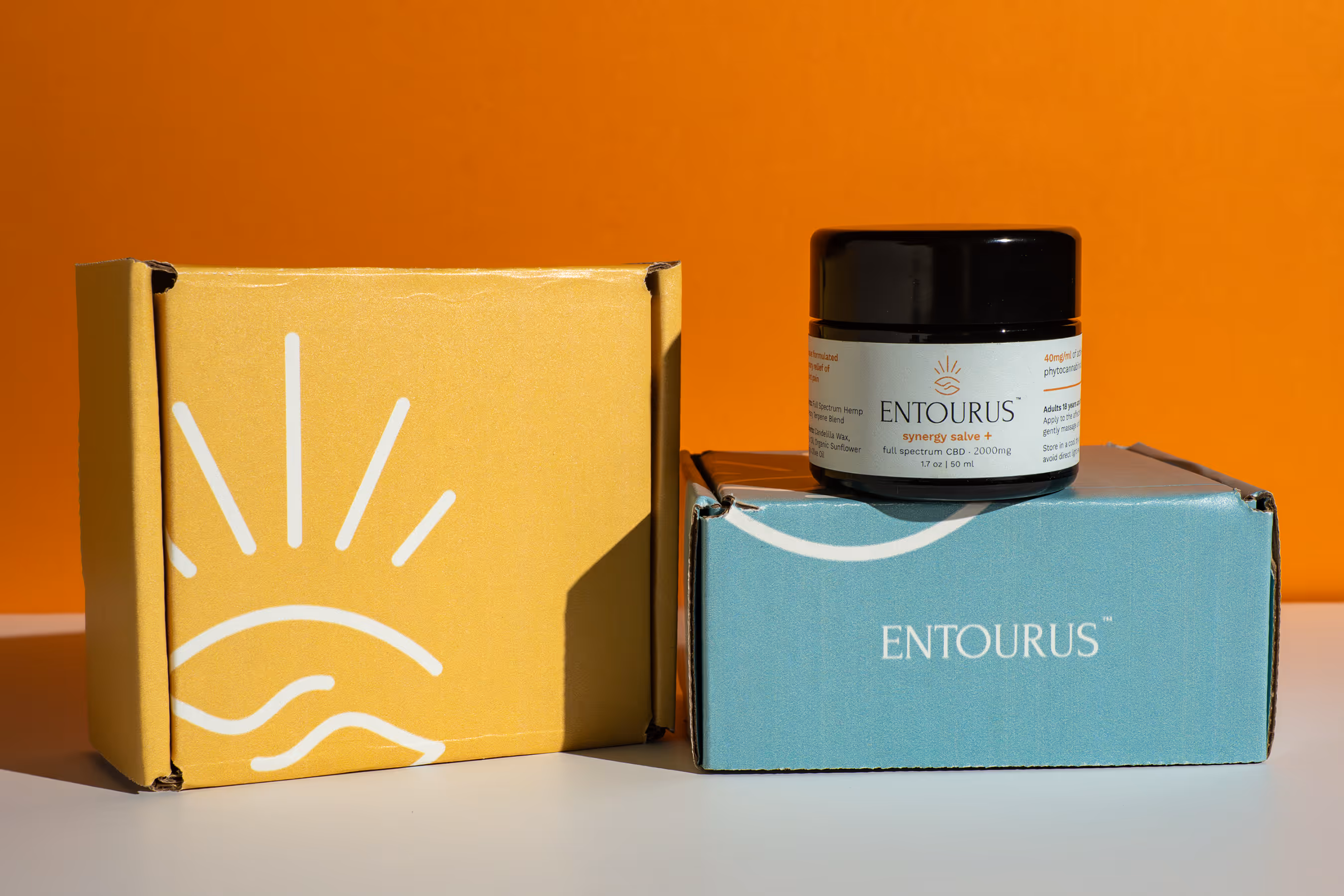 Entourus synergy salve jar on teal box beside yellow box on orange backdrop, product photography, Photos by Lars.