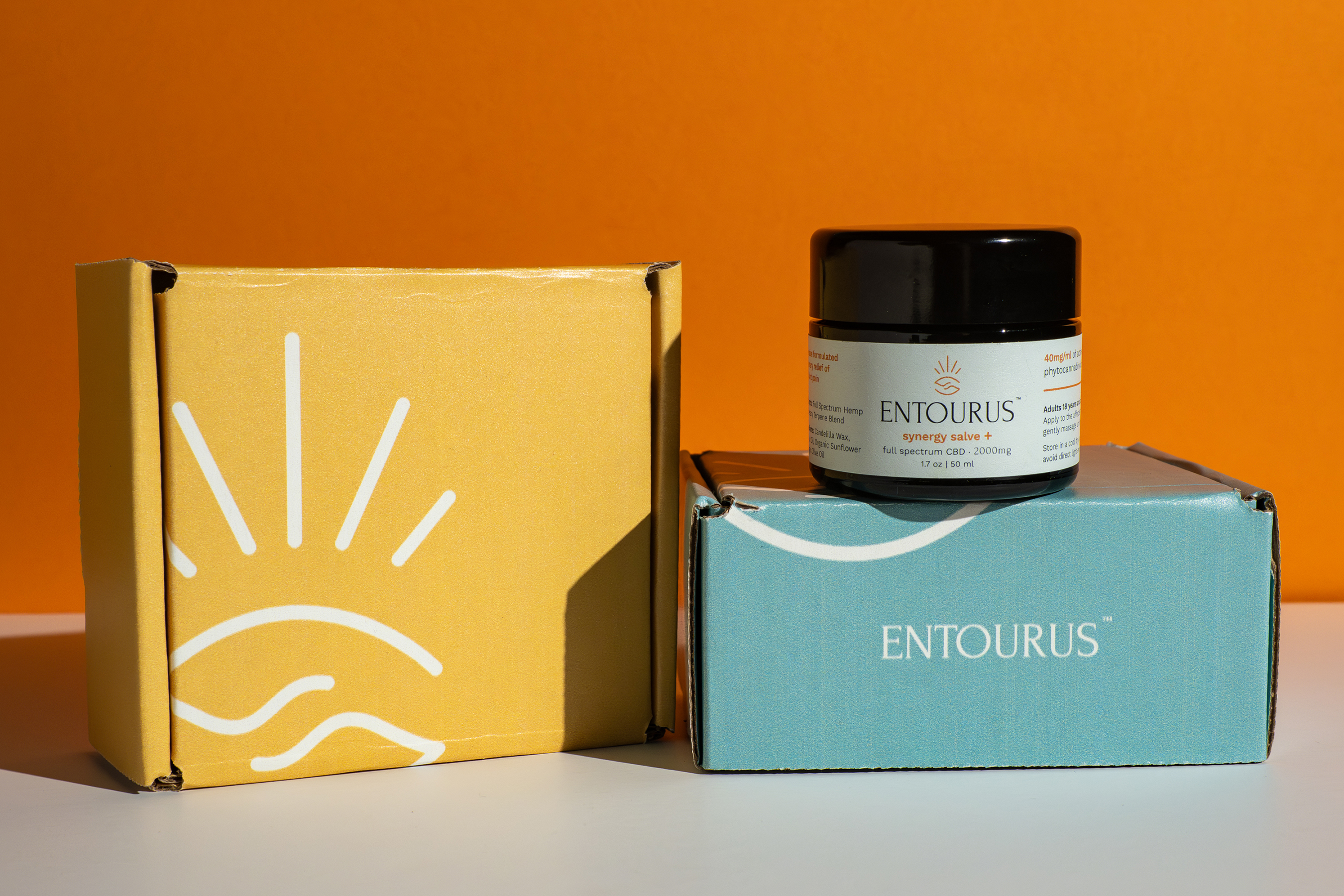 Entourus synergy salve jar on teal box beside yellow box on orange backdrop, product photography, Photos by Lars.