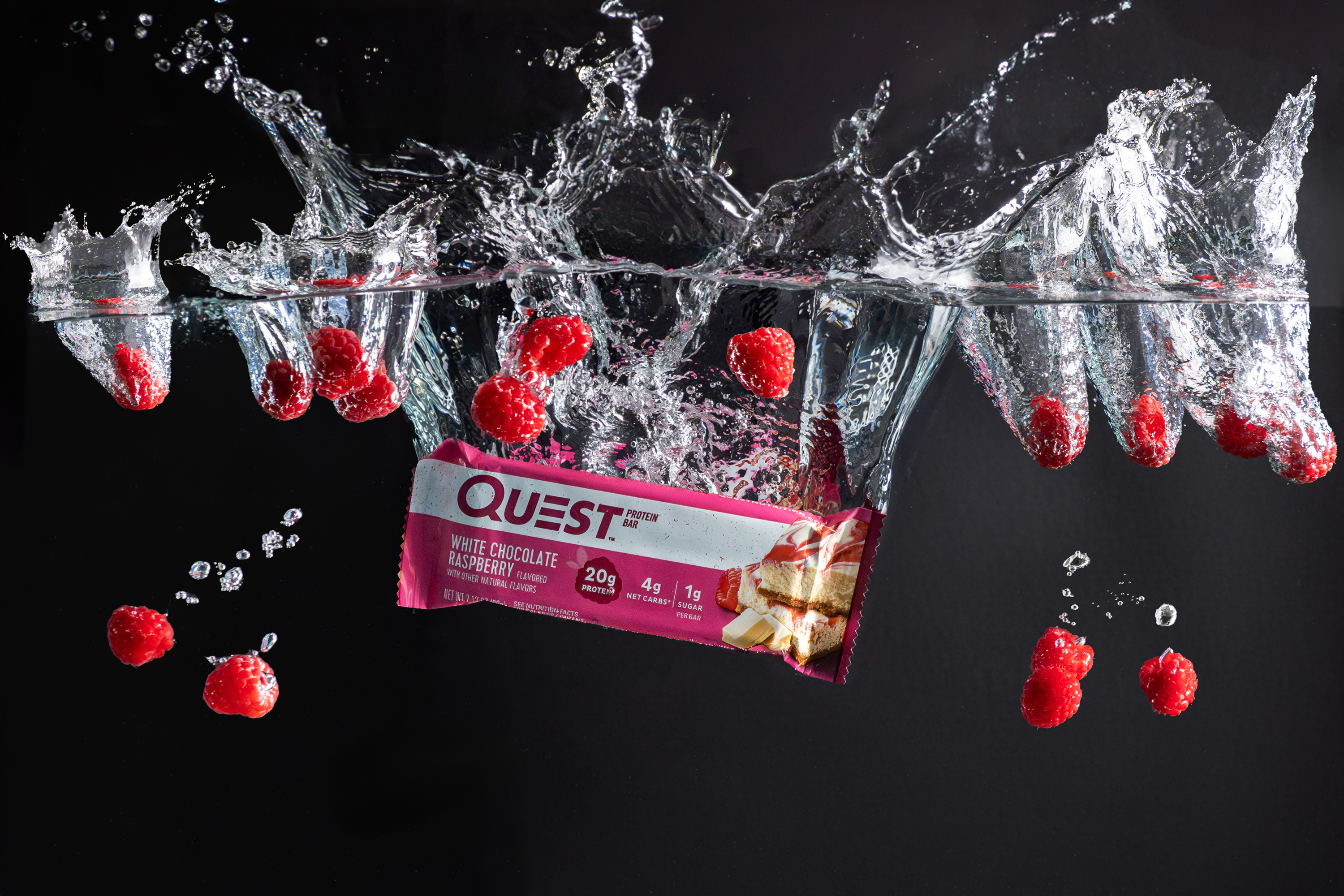Quest White Chocolate Raspberry protein bar splashing underwater with floating raspberries on black, food photography, Photos by Lars.