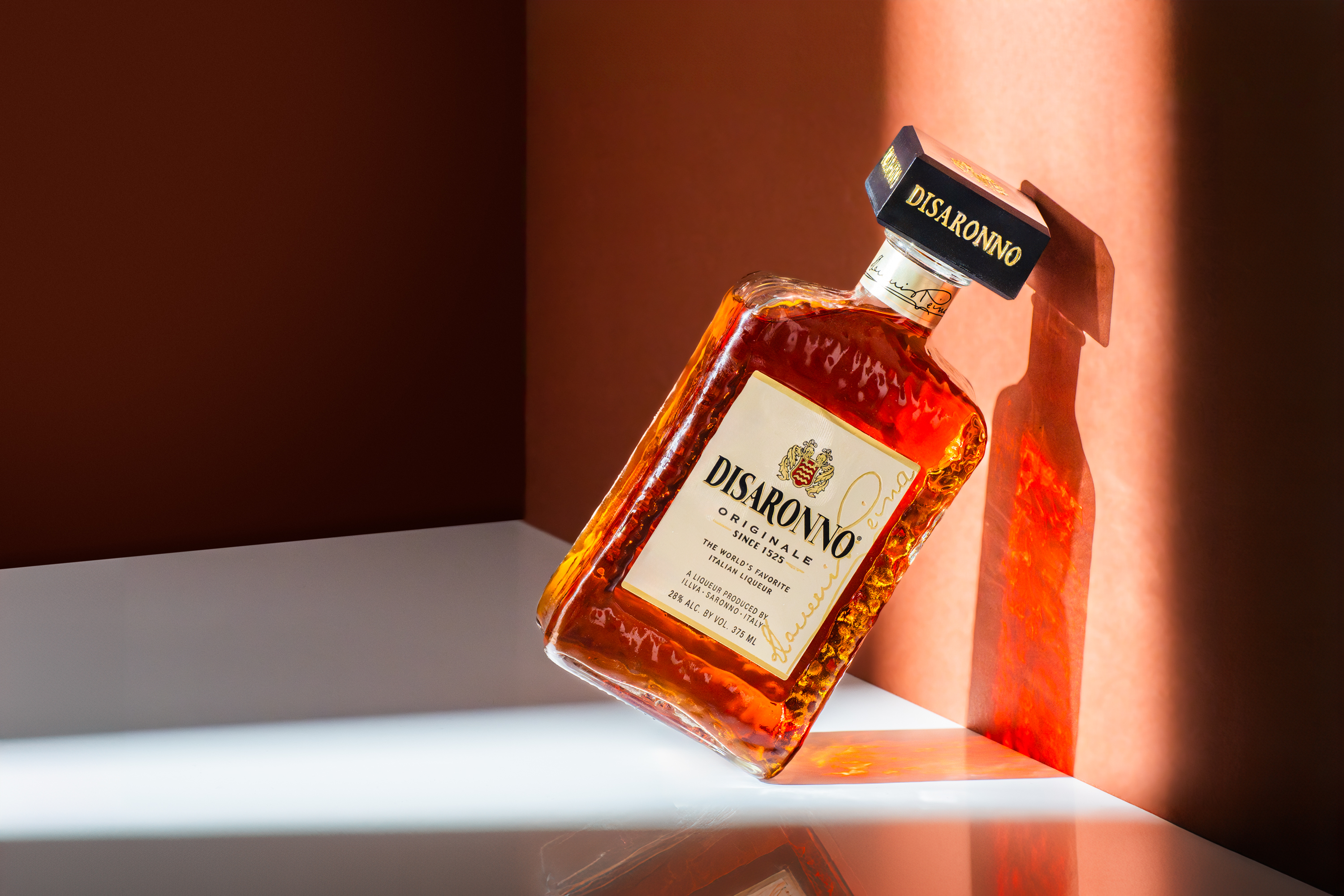Disaronno Originale bottle tilted in amber light casting shadow on wall, beverage photography, Photos by Lars.