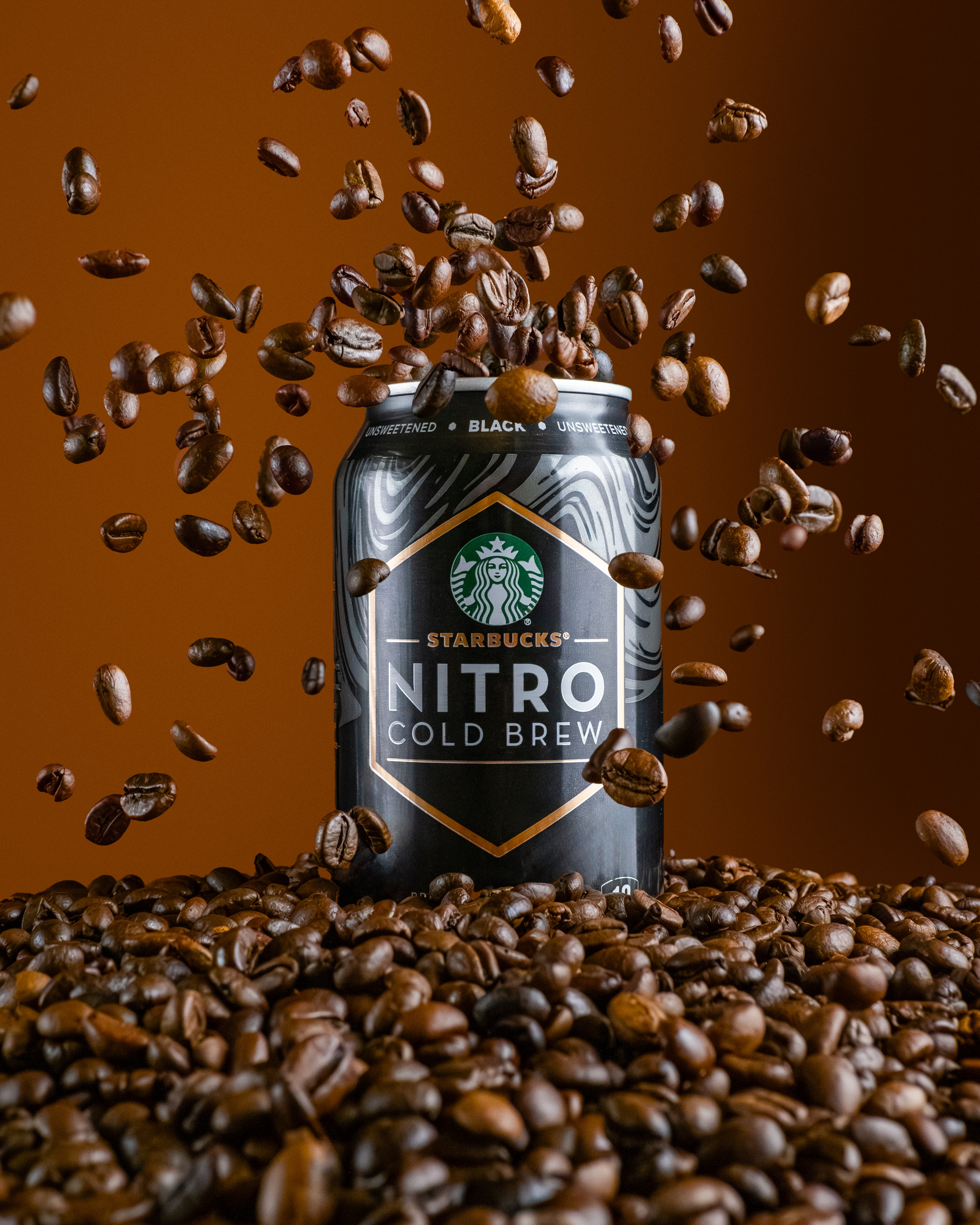 Starbucks Nitro Cold Brew can surrounded by coffee beans with beans falling, food photography, Photos by Lars.