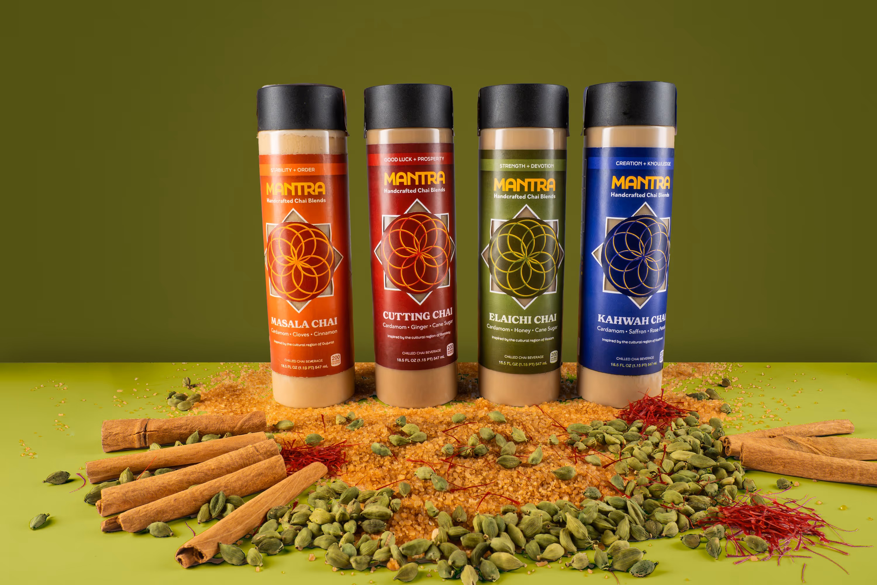 Mantra chai bottles lineup with cinnamon sticks, cardamom pods, saffron, and sugar on green backdrop, product photography, Photos by Lars.