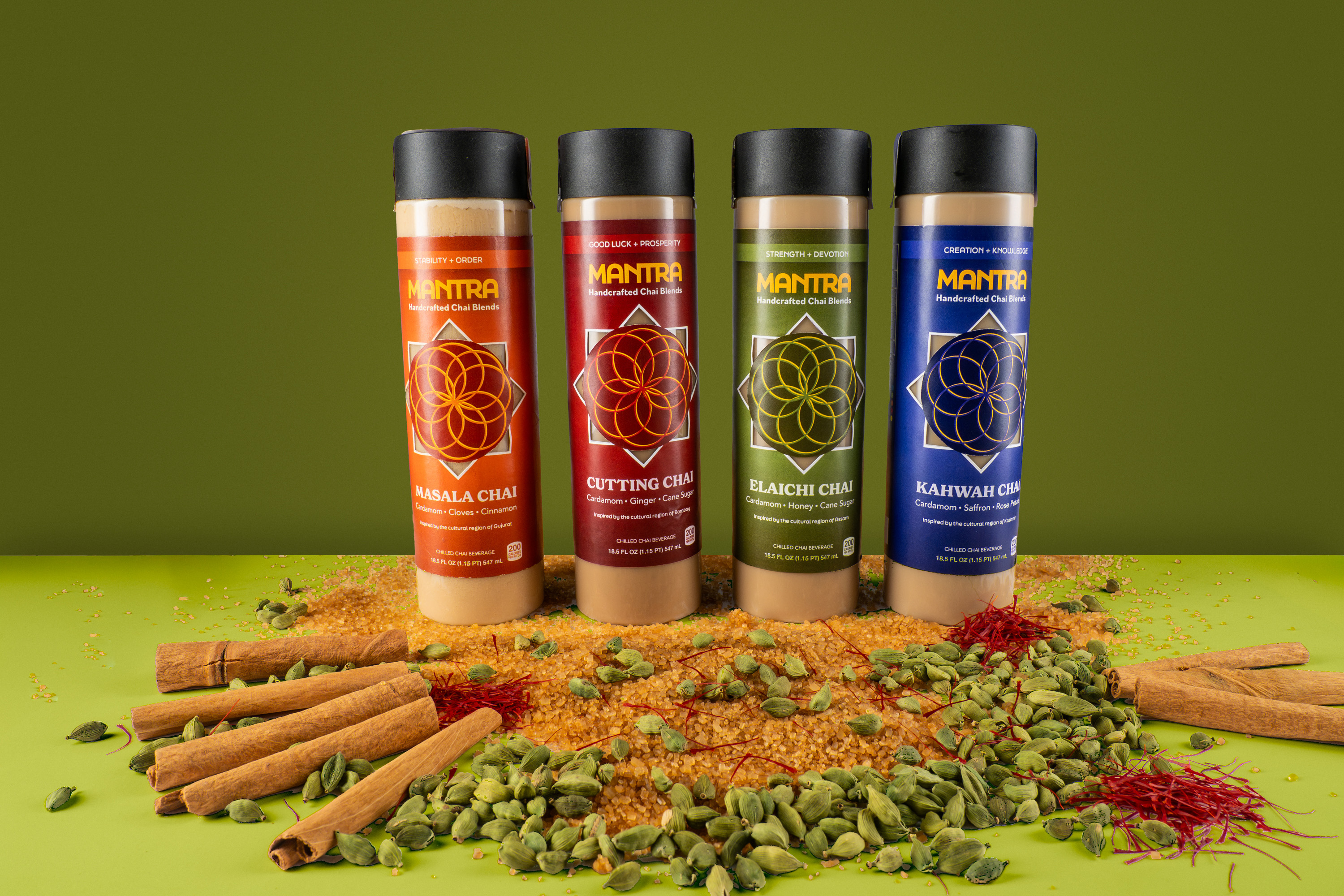 Mantra chai bottles lineup with cinnamon sticks, cardamom pods, saffron, and sugar on green backdrop, product photography, Photos by Lars.