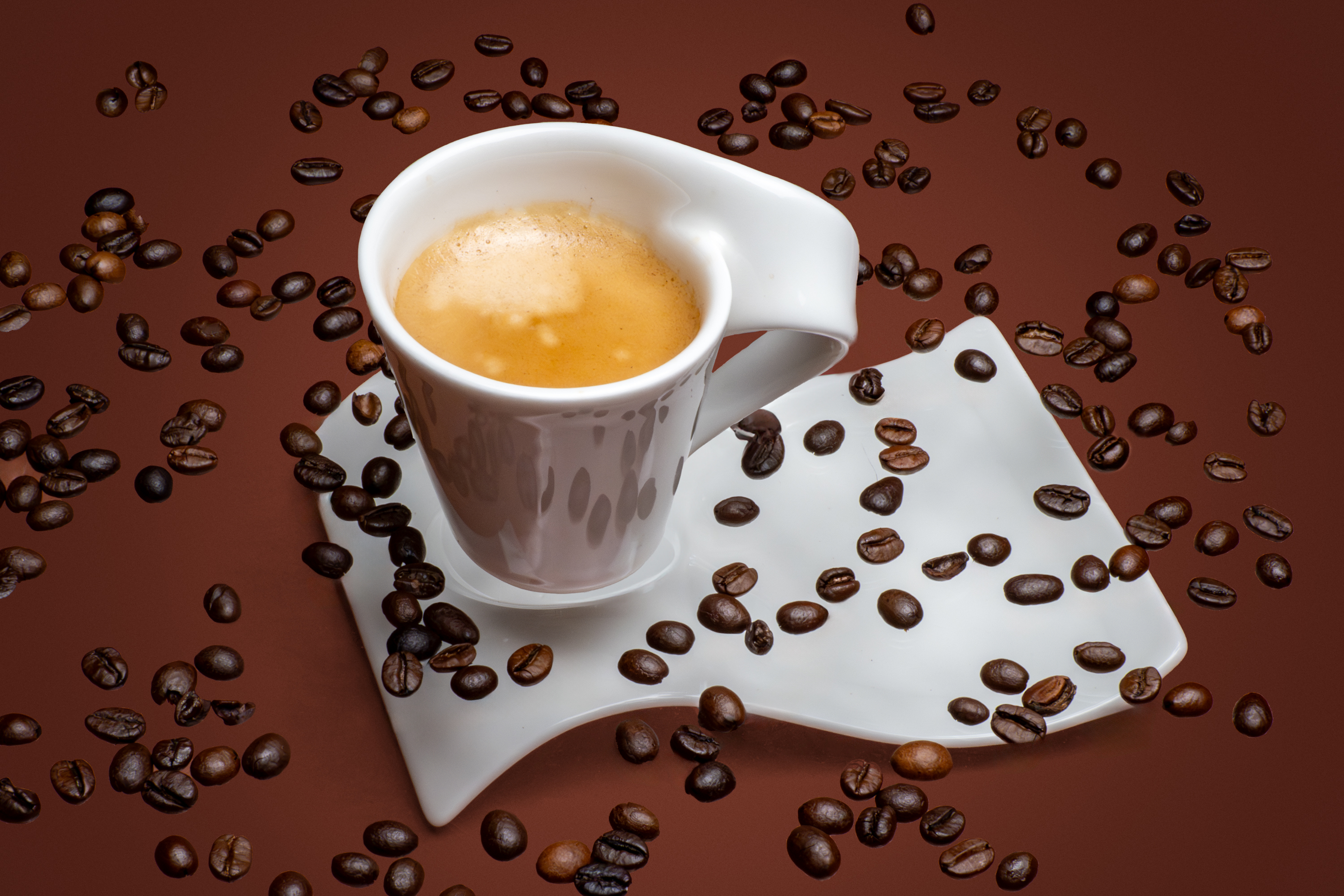 Espresso in a white cup on a saucer with scattered coffee beans on brown background, product-style food photo by Photos by Lars.