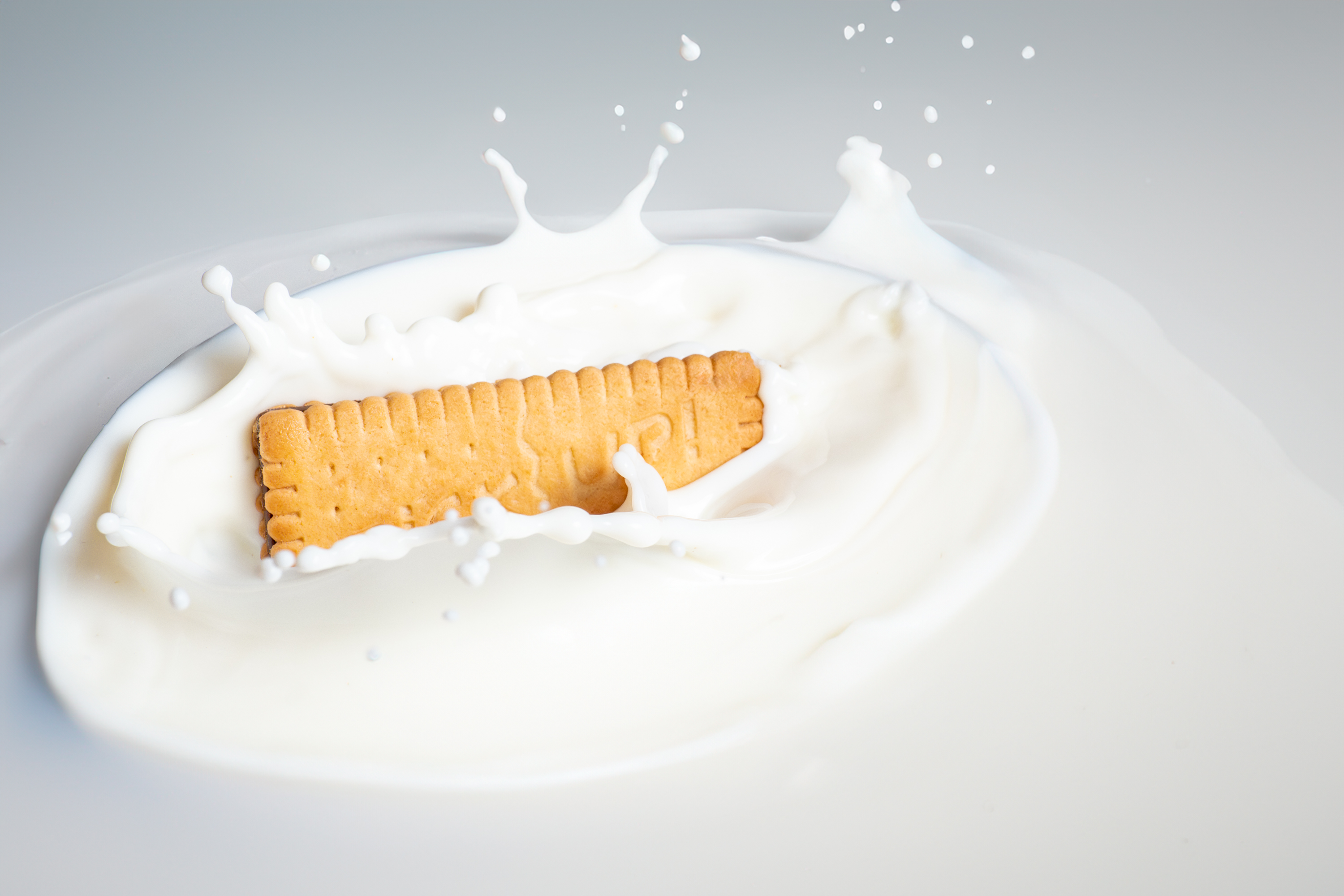 Biscuit splashing into milk with frozen droplets on a clean white background, high-speed food photo by Photos by Lars.