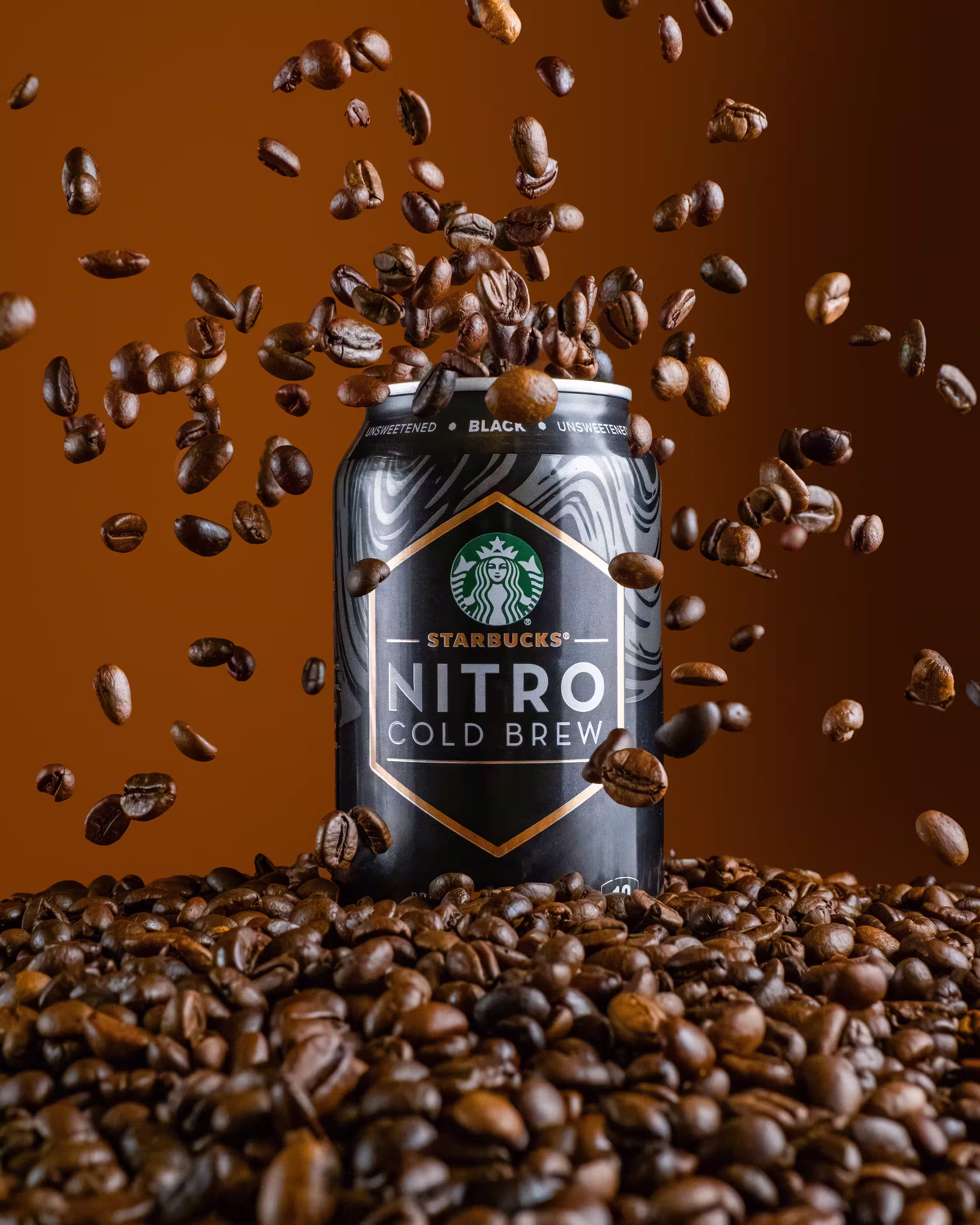 Starbucks Nitro Cold Brew can surrounded by flying coffee beans on brown background, product photography by Photos by Lars.