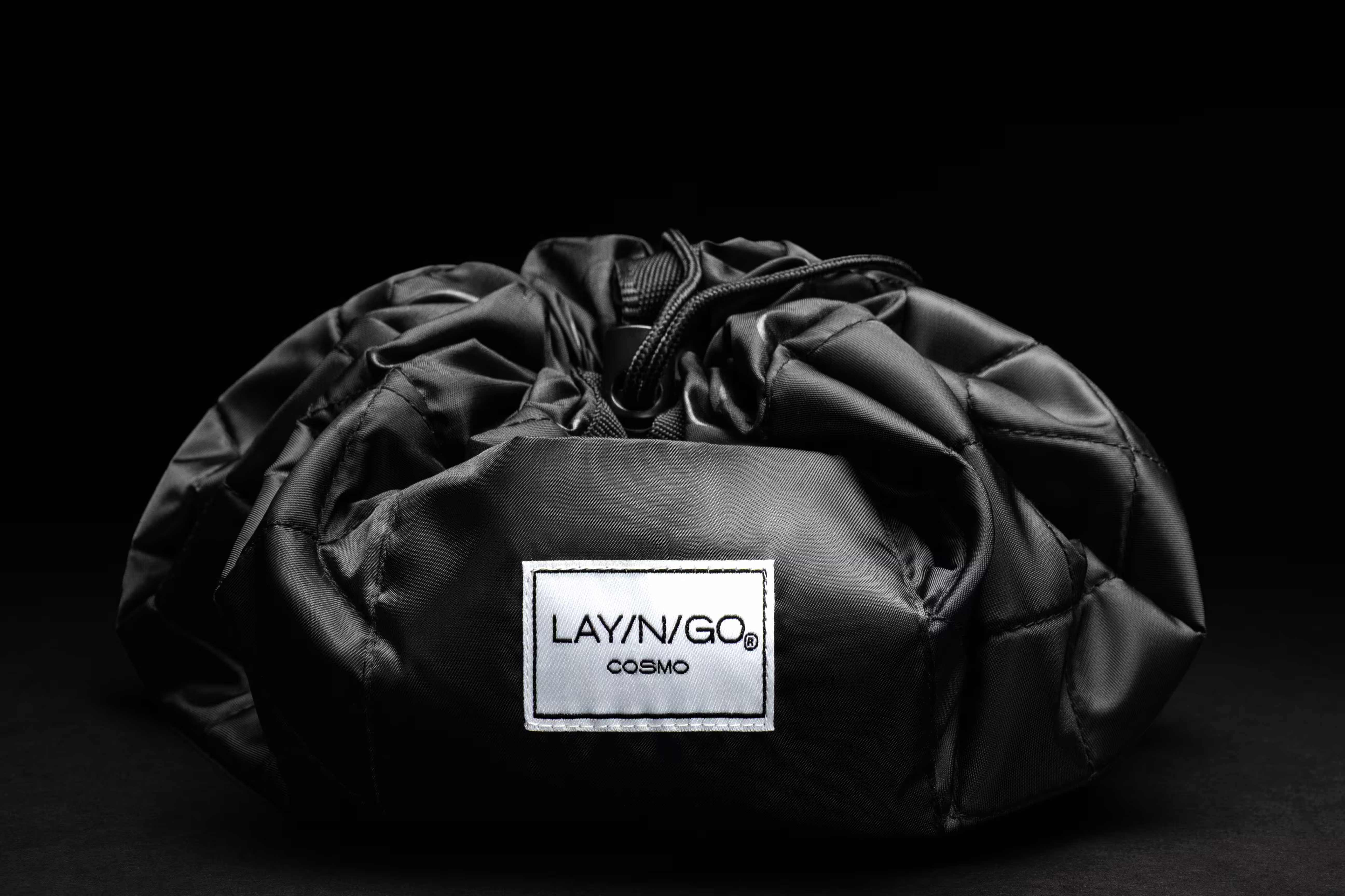 Lay-n-Go black drawstring makeup bag on dark background, ecommerce product photography by Photos by Lars.