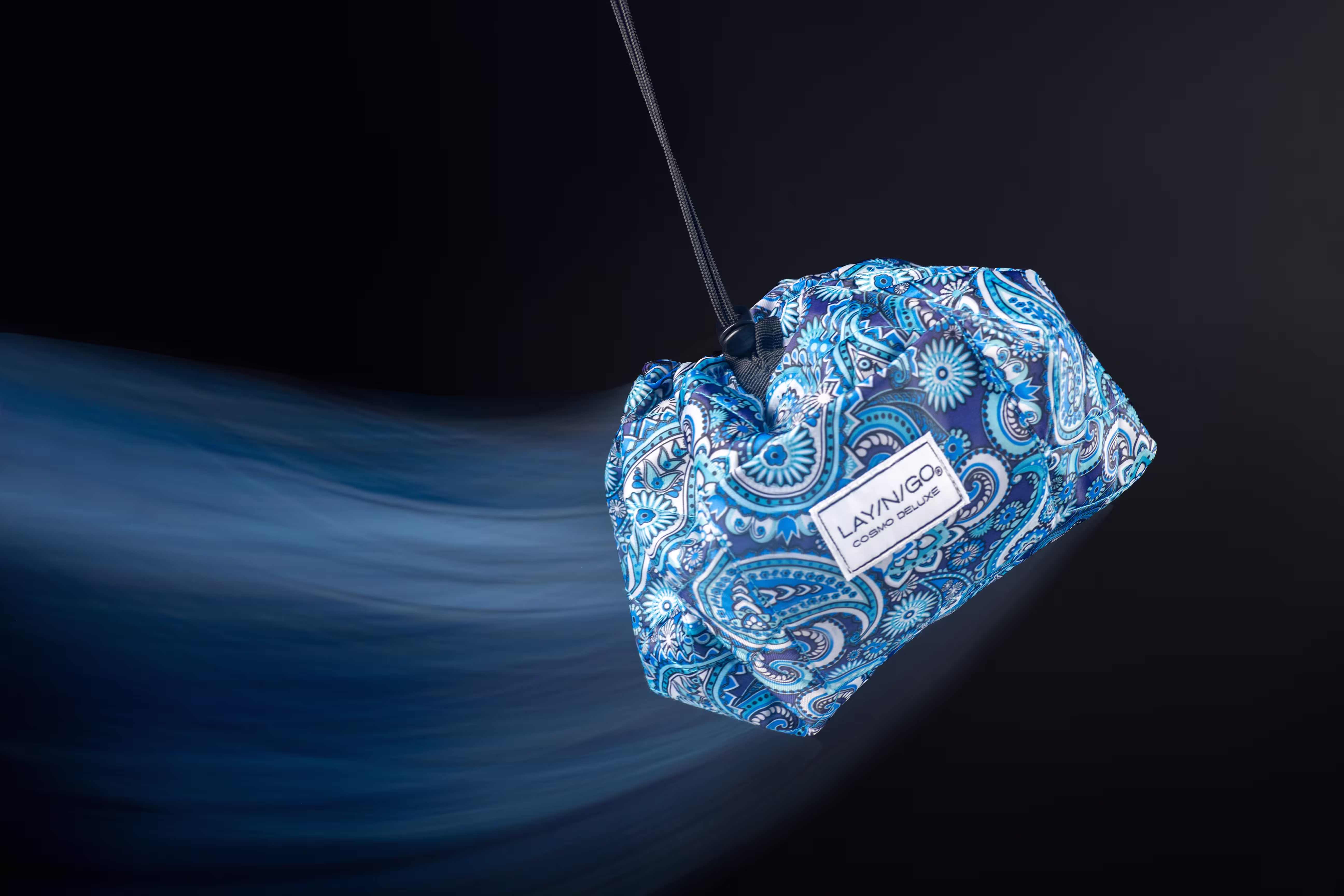 Blue Lay-n-Go makeup bag streaking through dark space with motion blur, studio product photography by Photos by Lars.