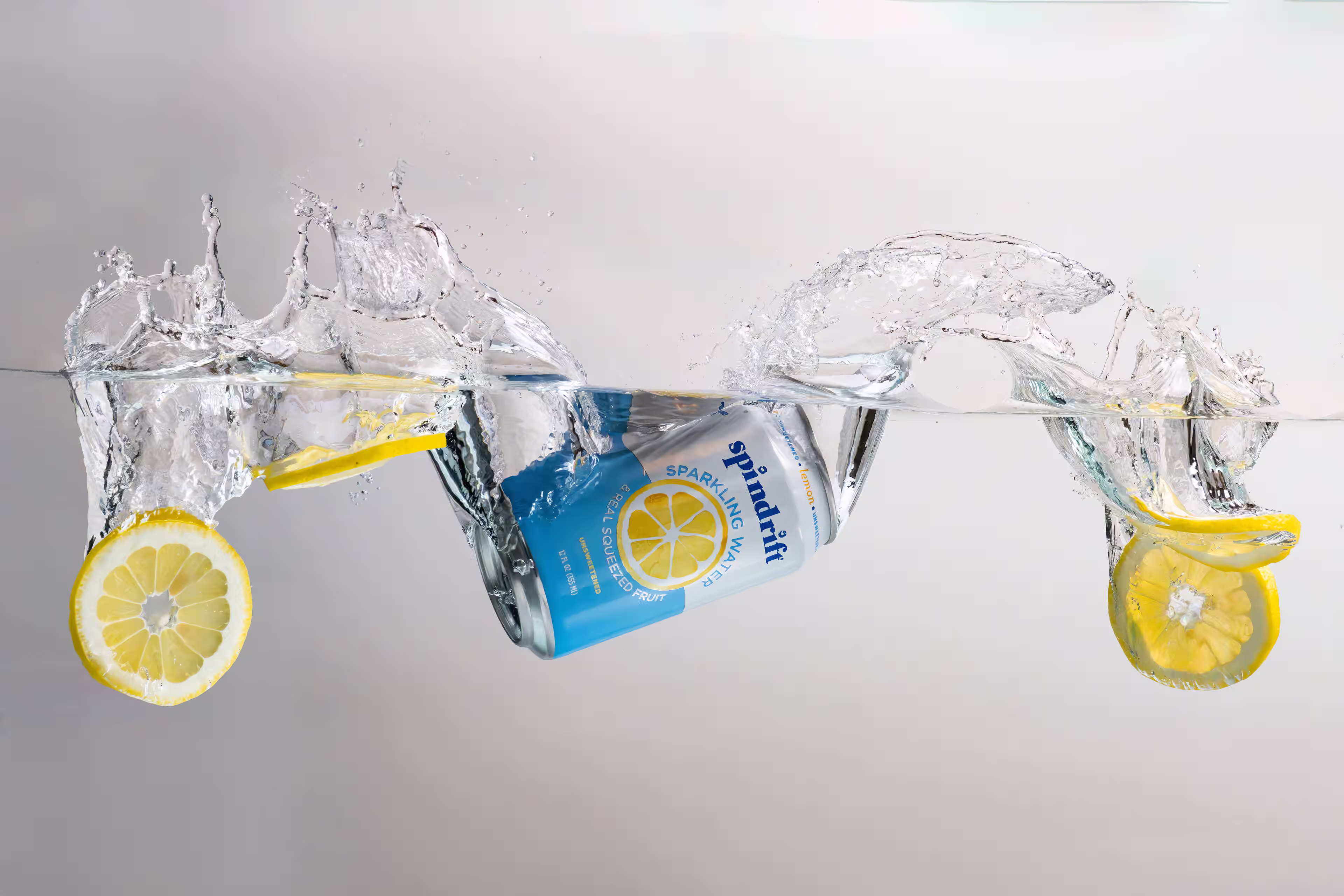 Spindrift sparkling water can splashing into water with lemon slices in a motion product photograph