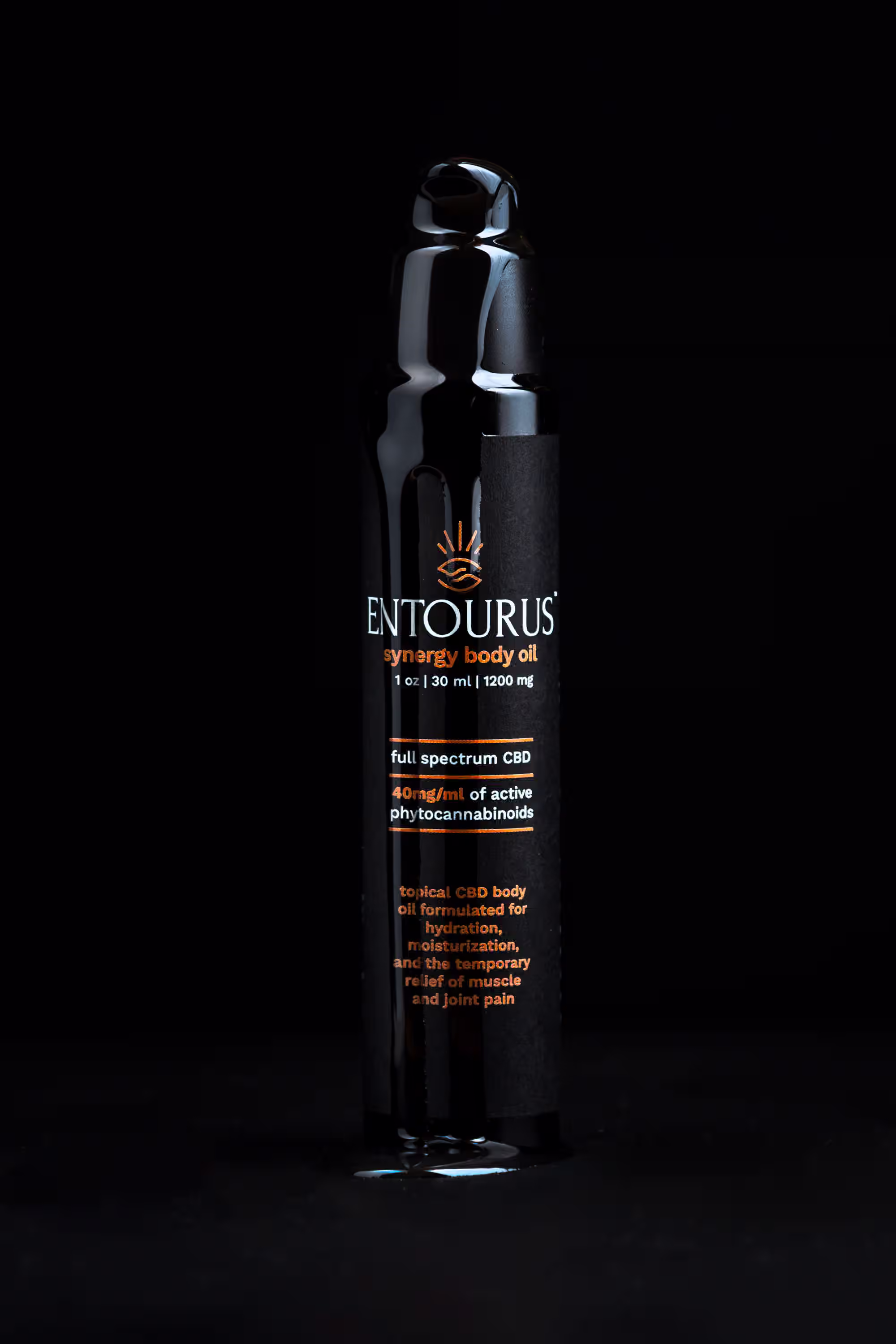 Entourus Synergy Body Oil bottle with oil dripping down the packaging in a dramatic motion product photograph on black background