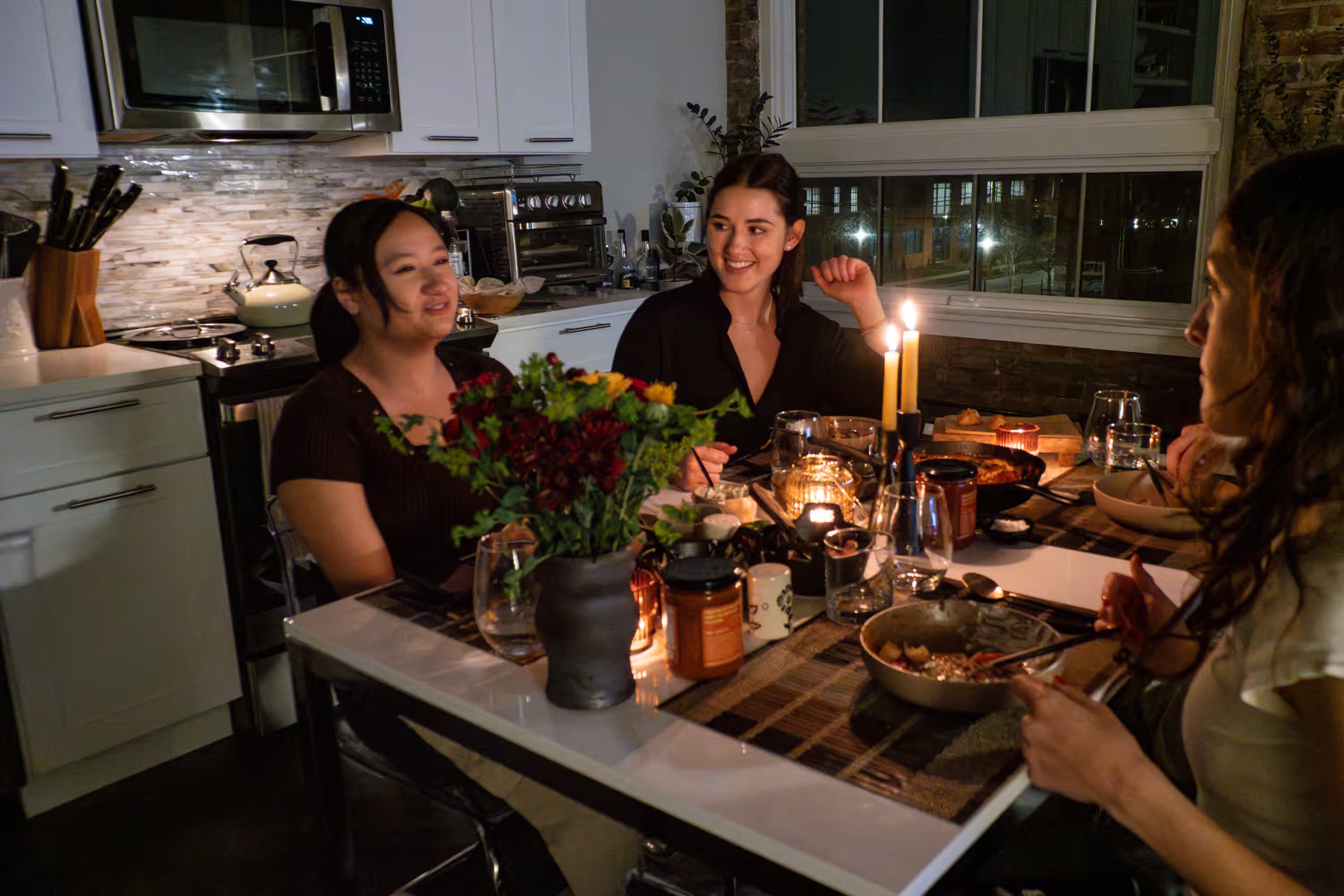Friends enjoying a candlelit dinner party with Shooka Sauce on the table in a lifestyle brand photograph