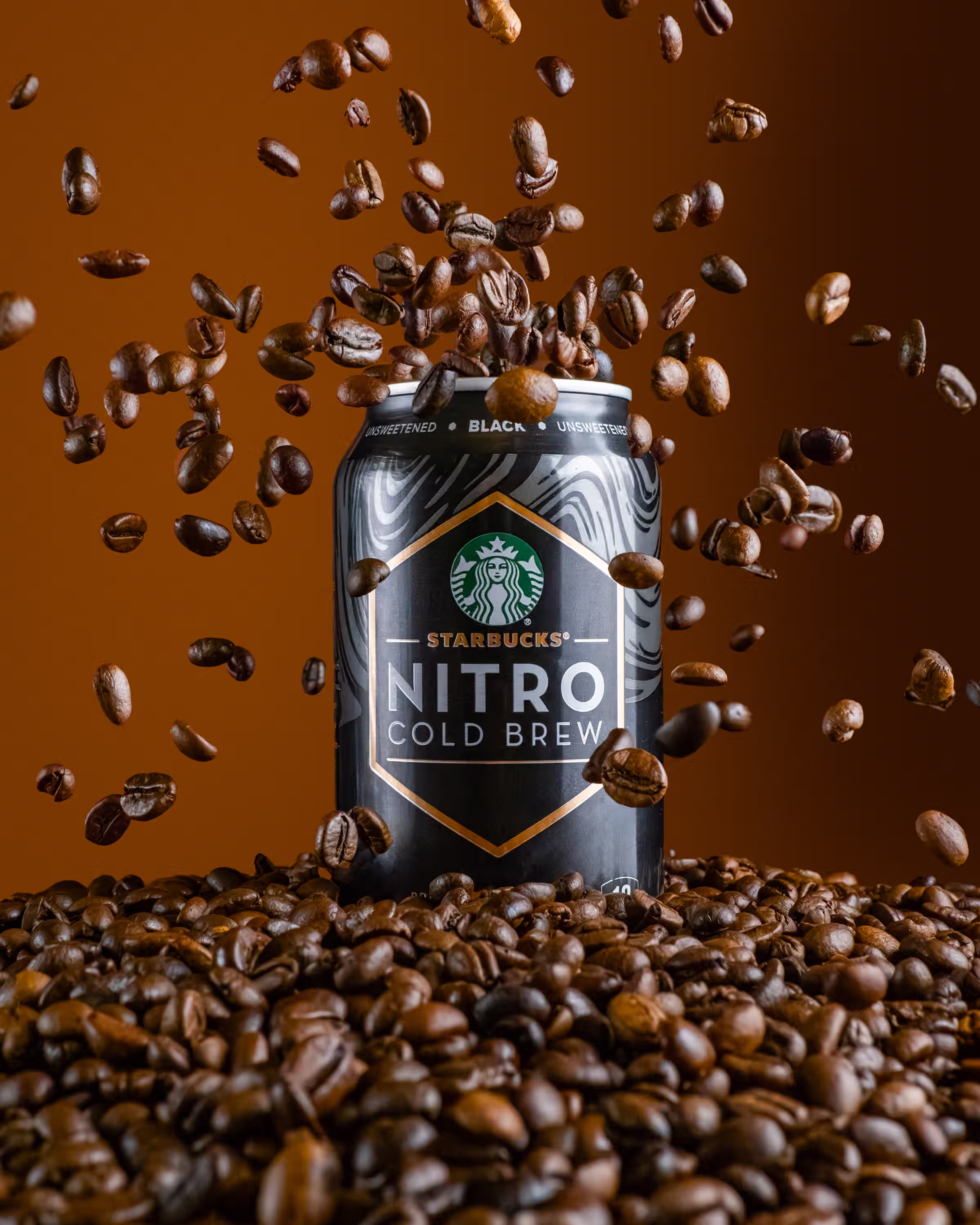 Starbucks Nitro Cold Brew can surrounded by coffee beans mid-air in a motion product photograph with warm studio lighting
