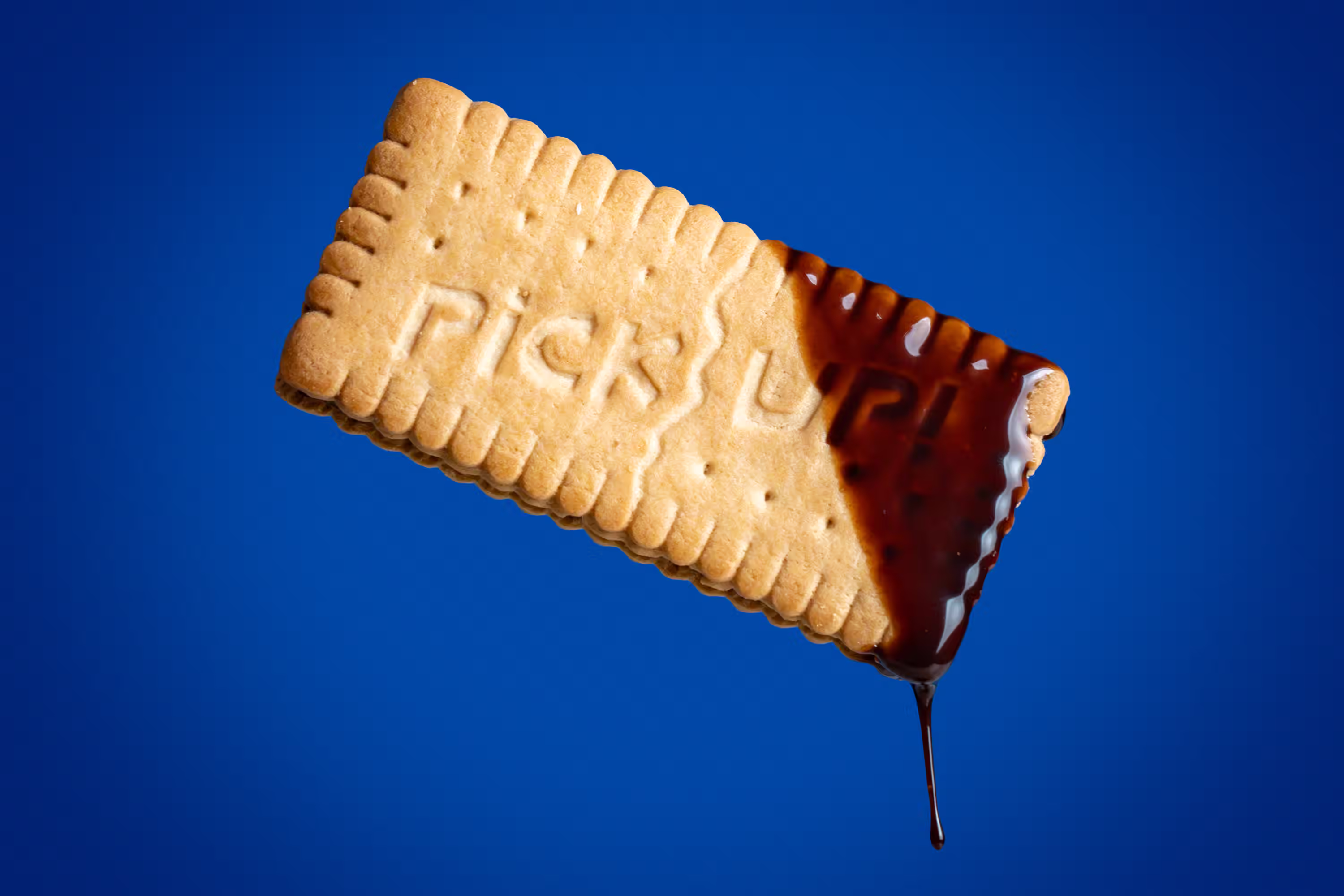 Pick Up biscuit floating at an angle with chocolate dripping from the corner against a blue background in a motion product photograph